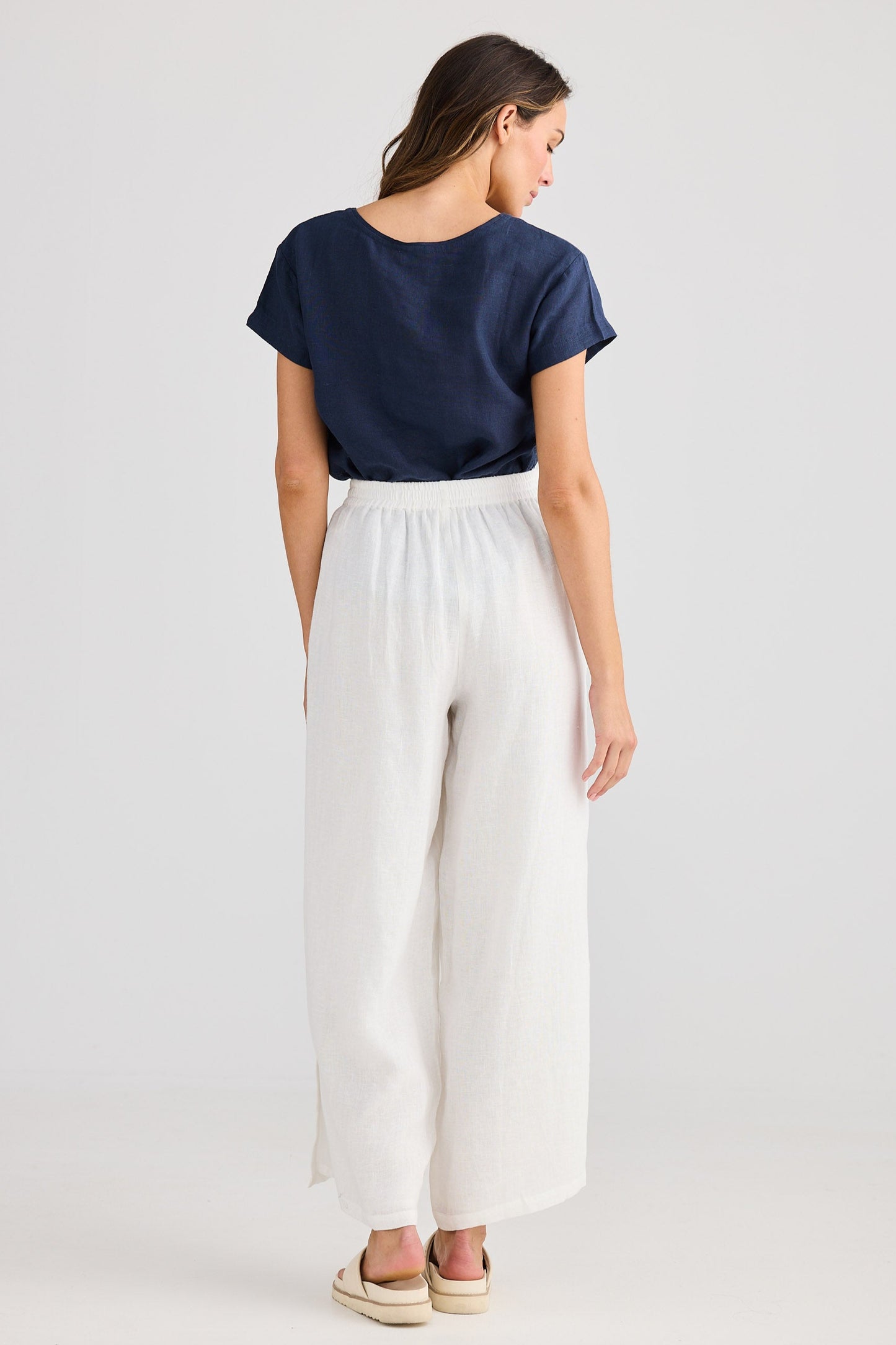 Woman wearing a navy top and white pants on a light gray background