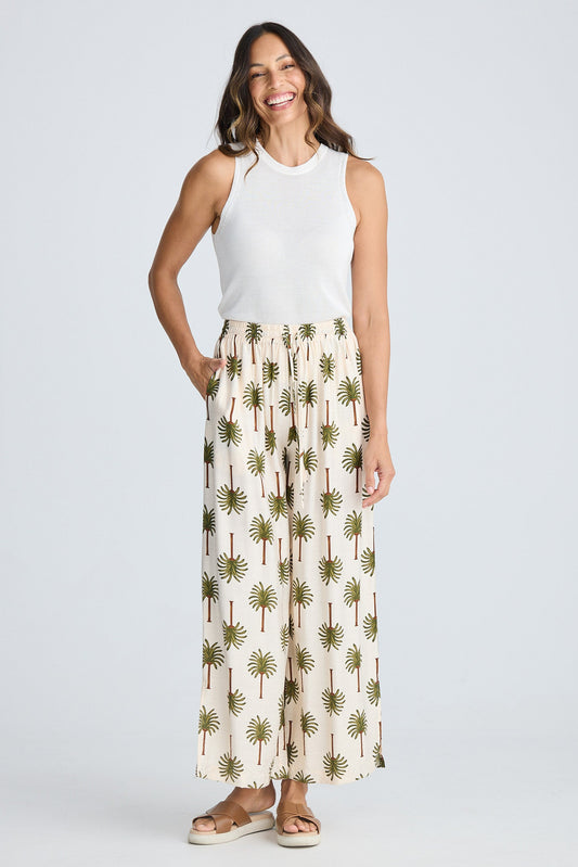 Woman wearing a white sleeveless top and palm tree patterned pants on a white background