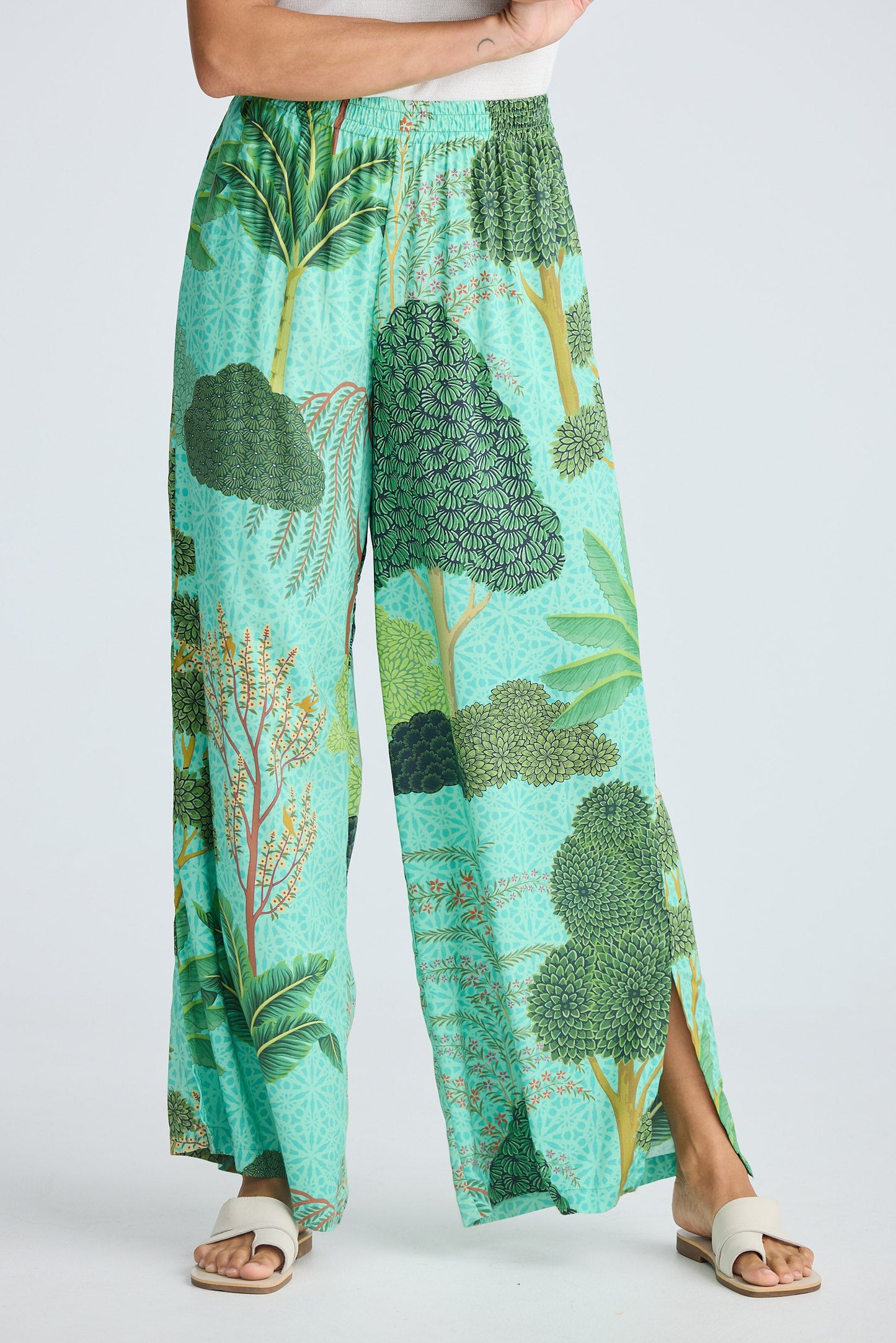 Person wearing a pair of wide-leg pants with a green leaf pattern on a white background