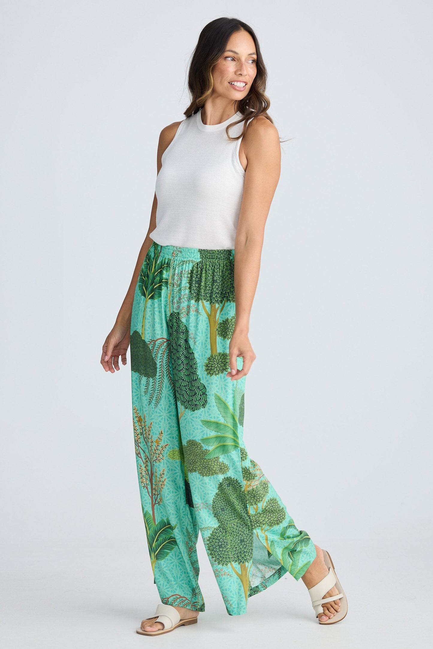 Woman wearing a white sleeveless top and green leaf-patterned pants on a white background