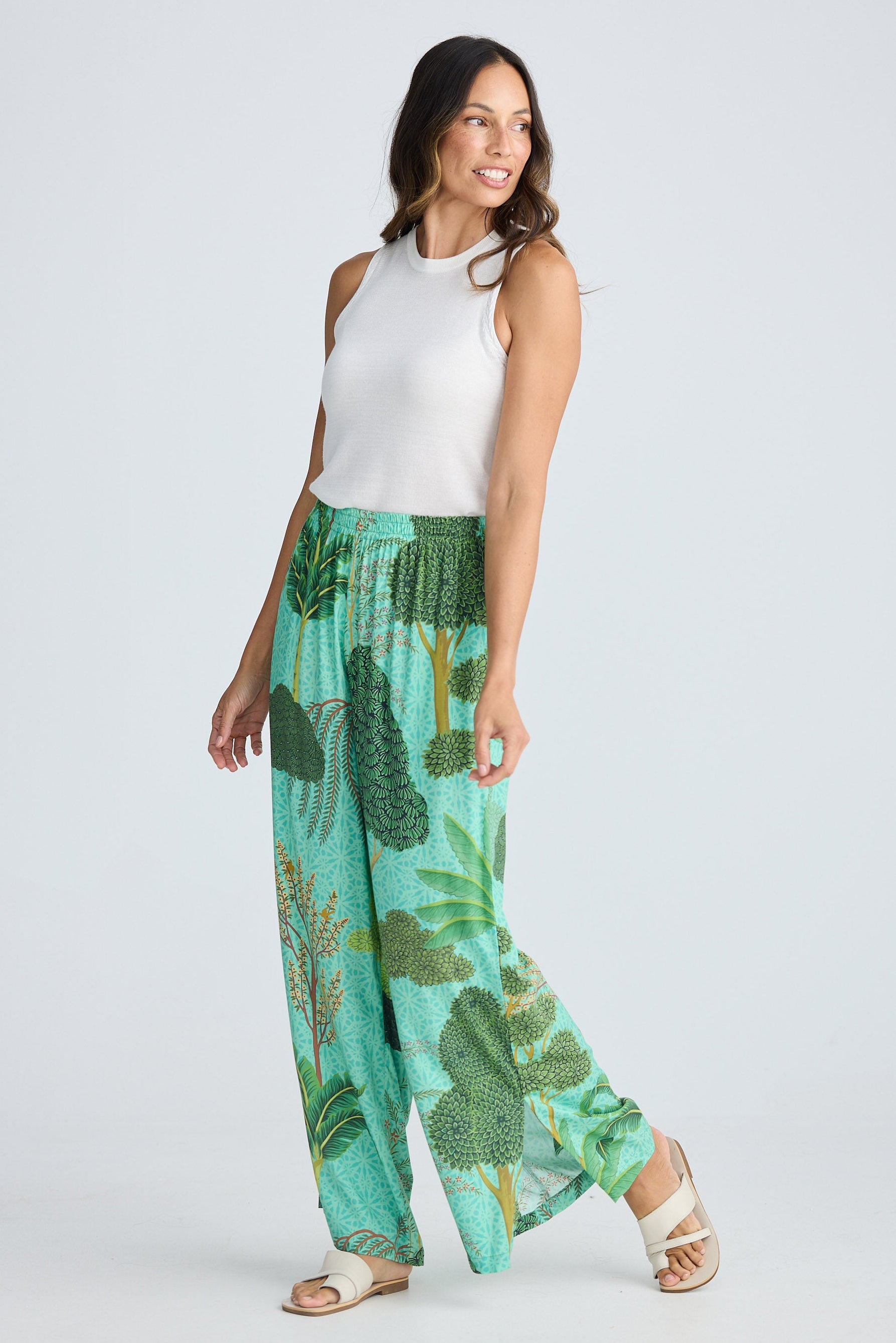 Woman wearing a white sleeveless top and green leaf-patterned pants on a white background
