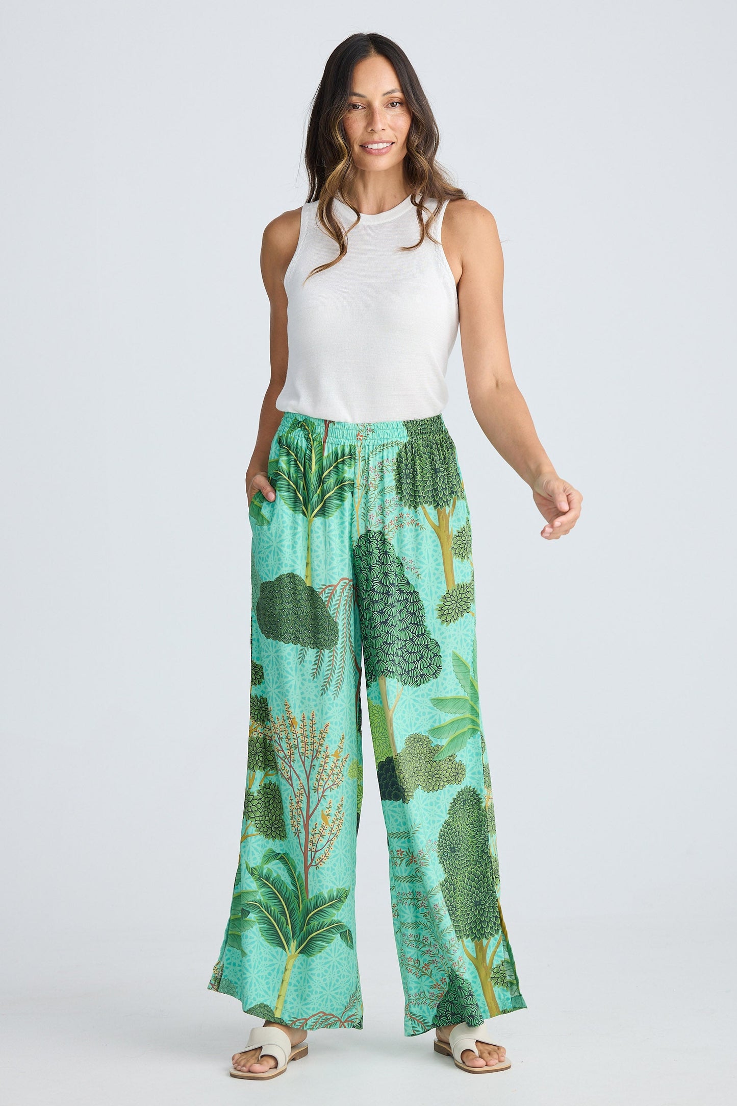 Woman wearing a white sleeveless top and green leaf-patterned pants on a white background