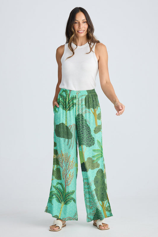 Woman wearing a white sleeveless top and green leaf-patterned pants on a white background