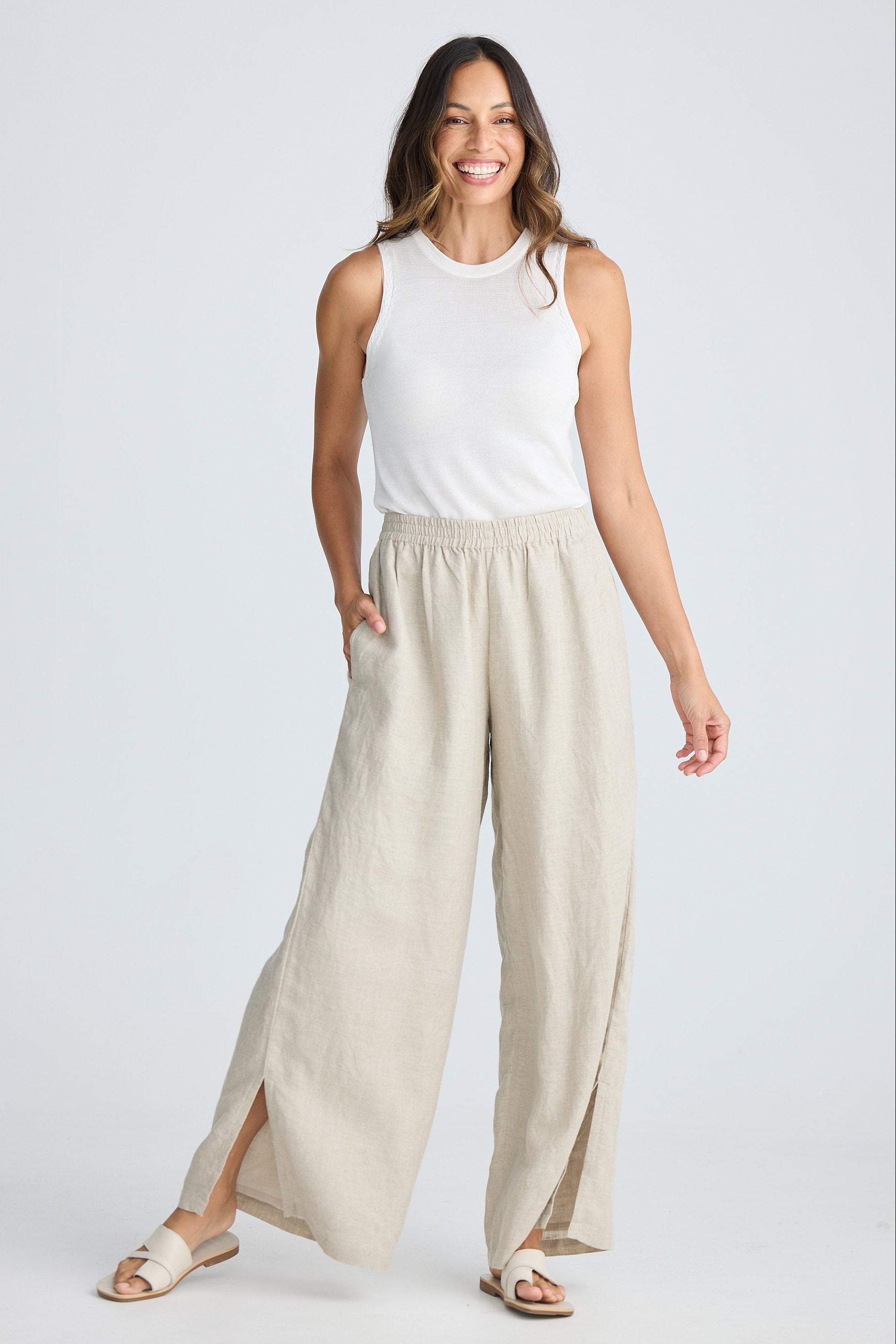 Woman wearing a white sleeveless top and beige wide-leg pants on a white background