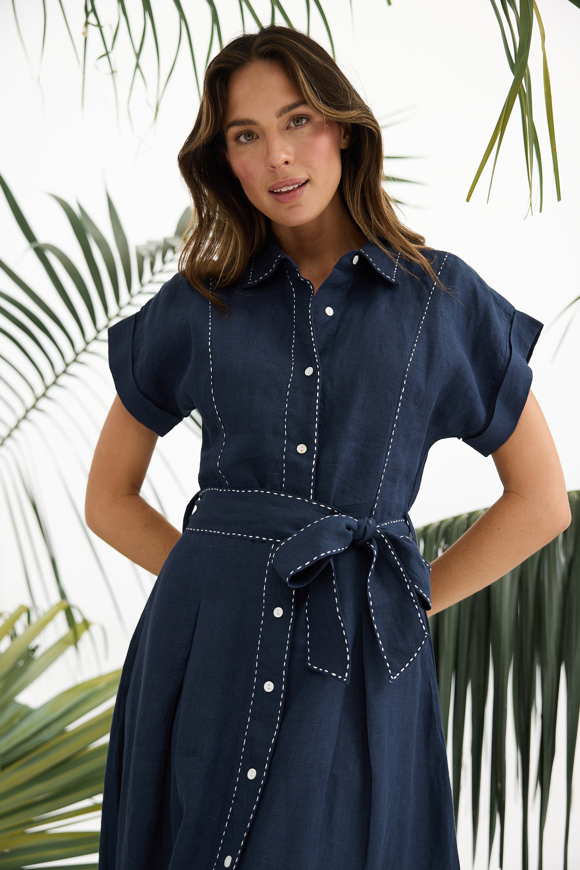 Woman wearing a navy dress with white buttons against a leafy background