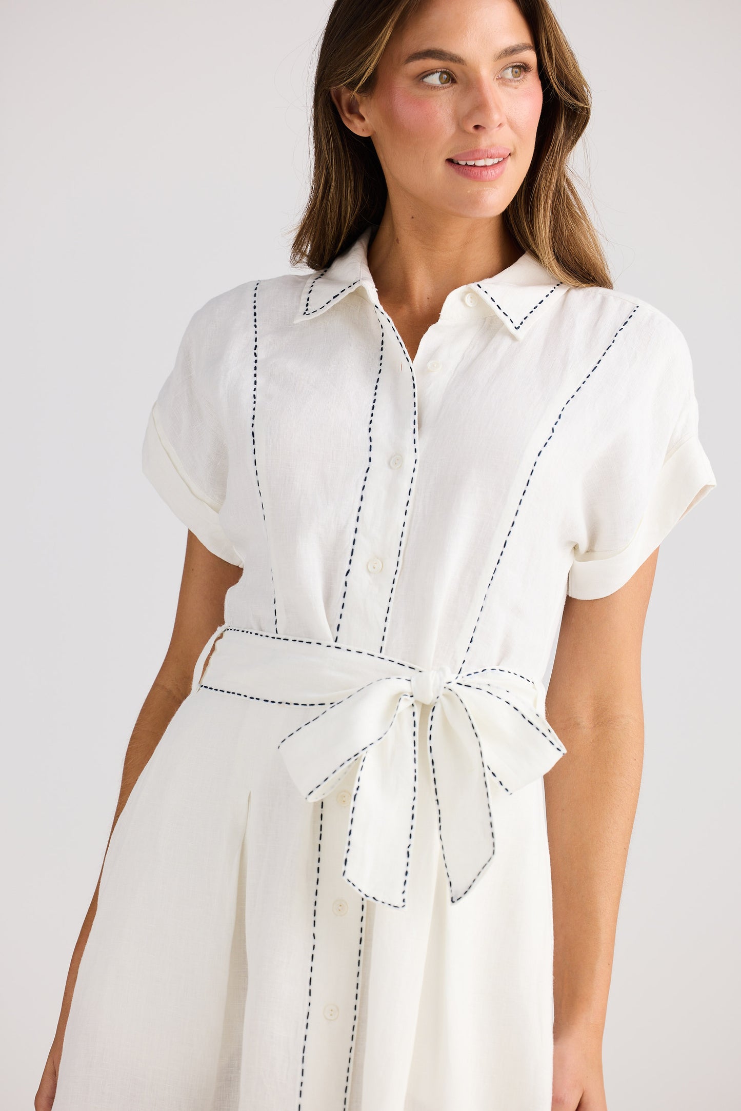 Woman wearing a white dress with black stitching on a plain background