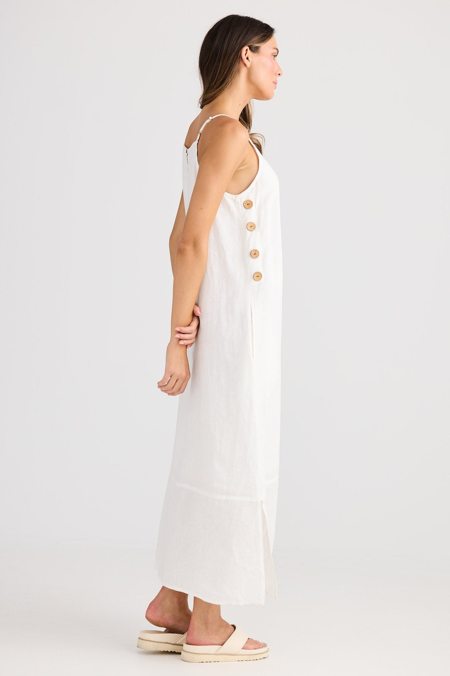 Woman wearing a white dress with gold buttons on a plain background