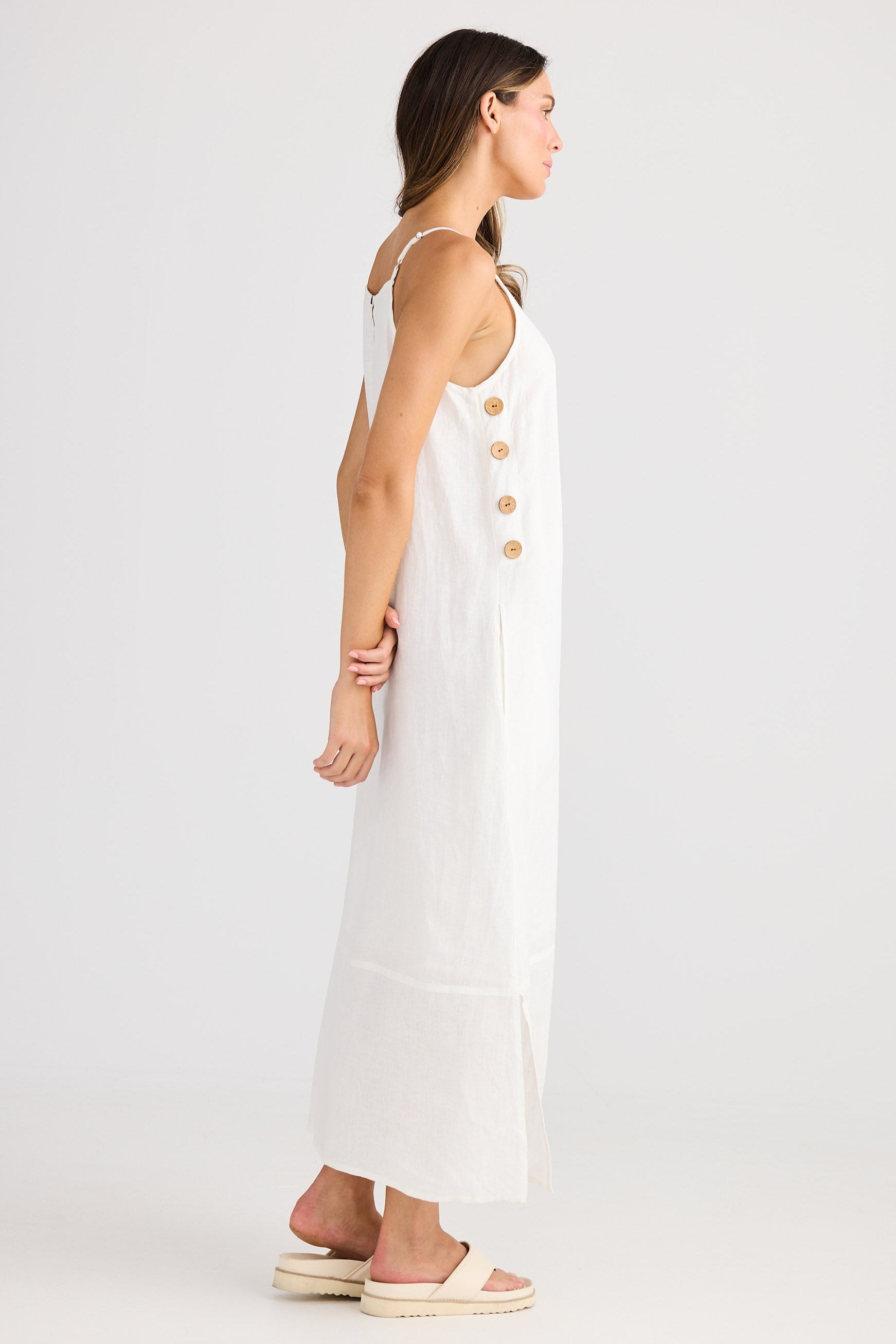 Woman wearing a white dress with gold buttons on a plain background