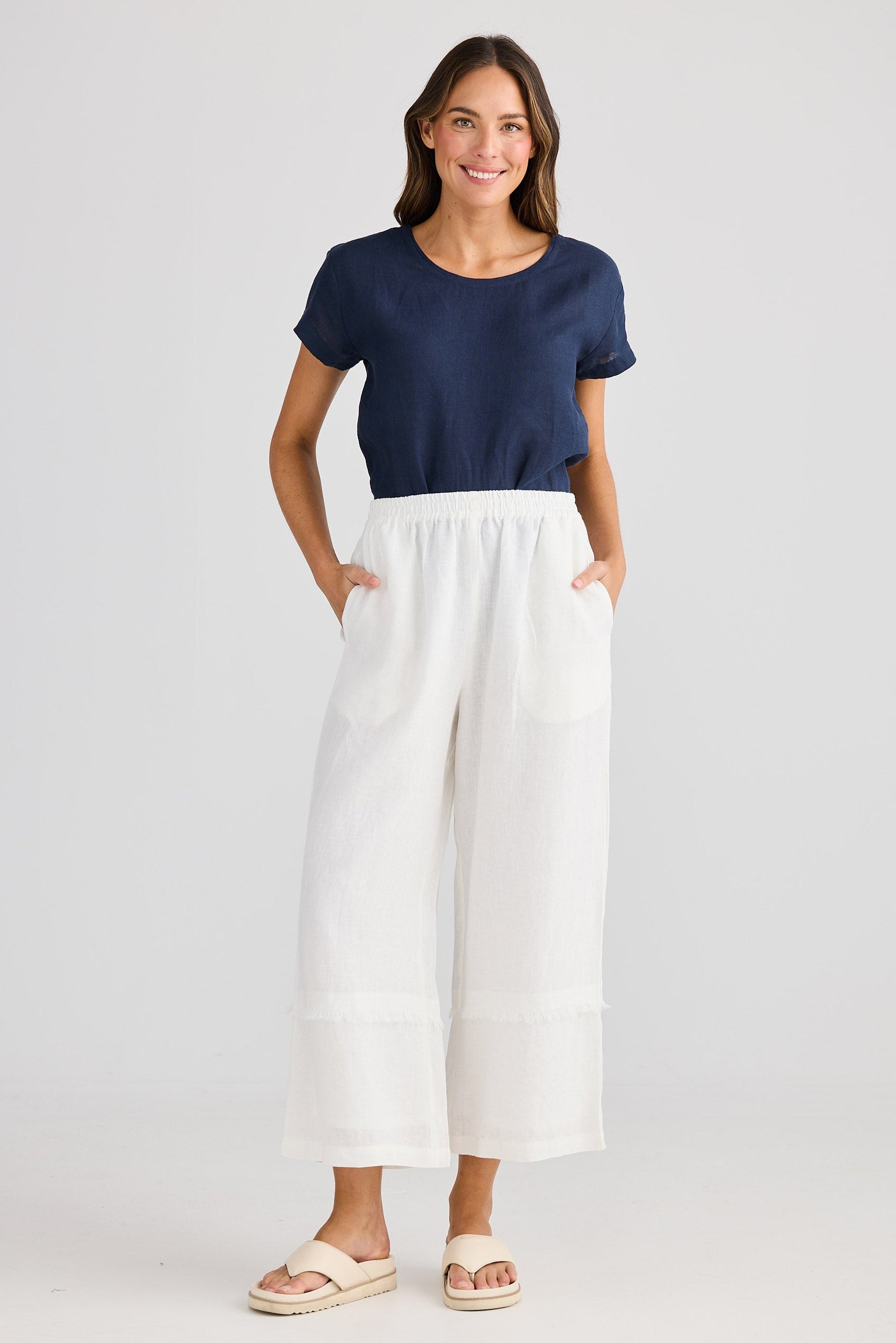 Woman wearing a navy top and white pants on a light gray background