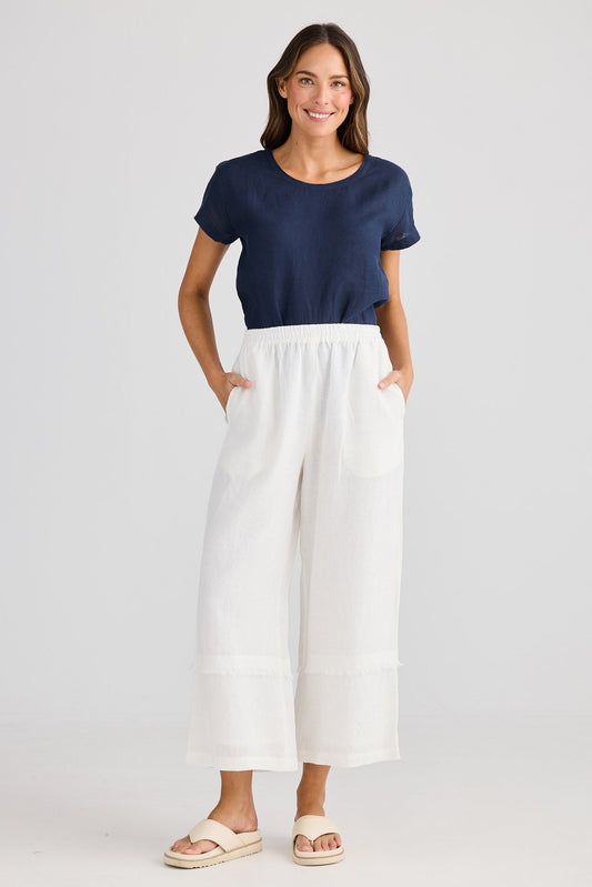 Woman wearing a navy top and white pants on a light gray background