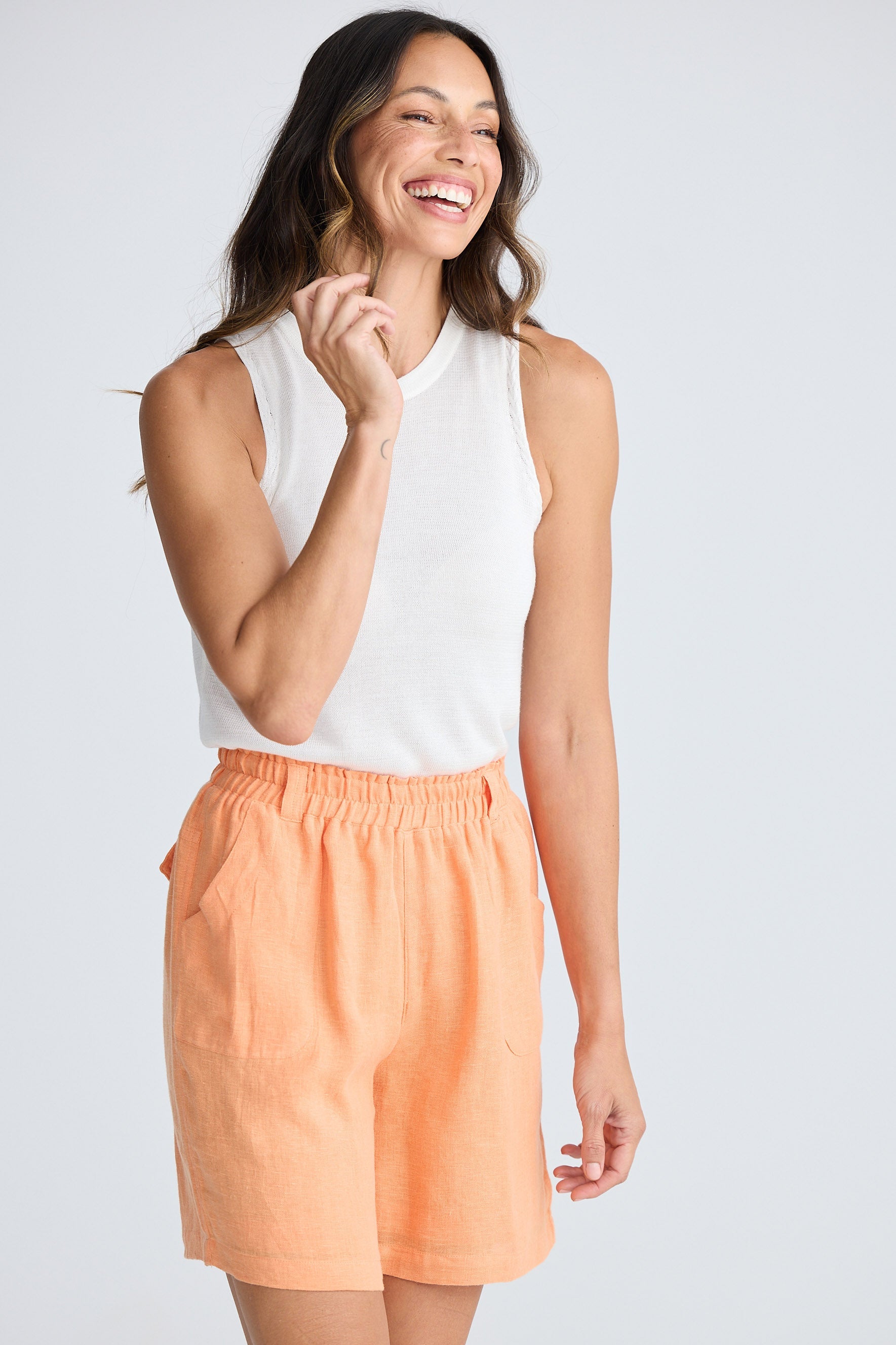 Woman wearing a white sleeveless top and peach shorts on a light gray background
