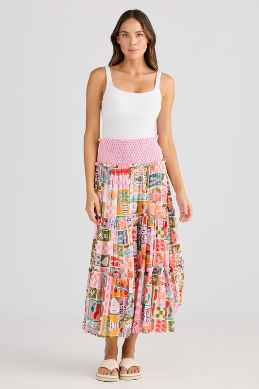 Woman wearing a colorful patterned skirt and white top on a plain background
