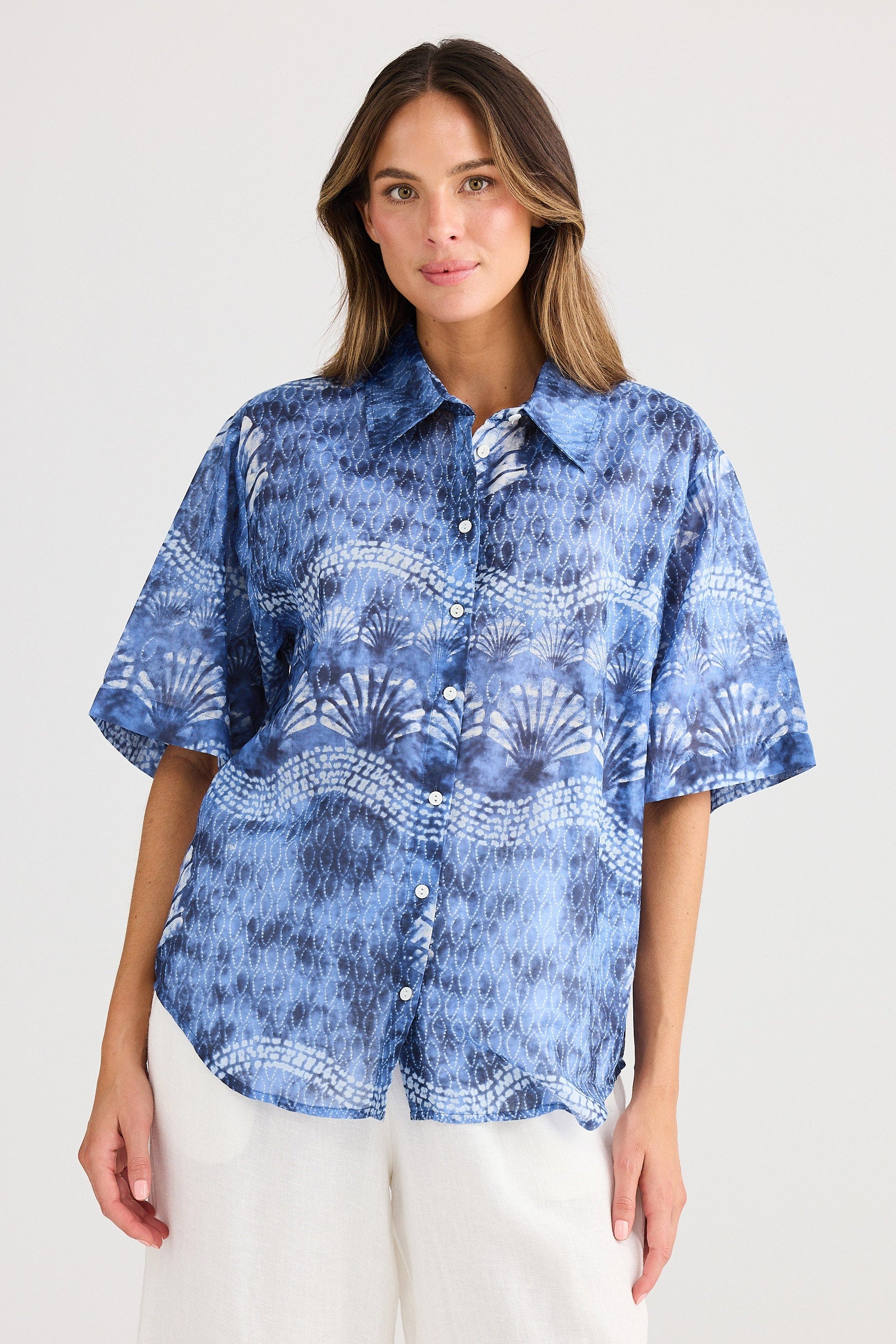 Woman wearing a blue patterned shirt with white pants on a light gray background