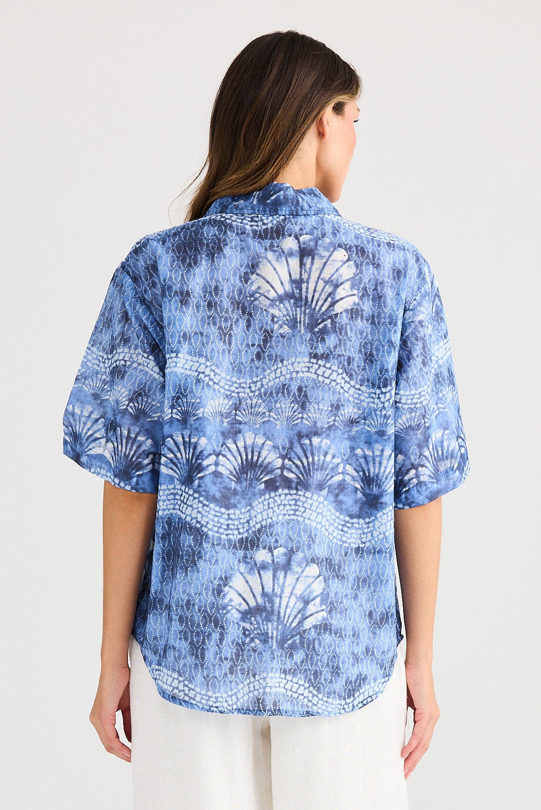 Woman wearing a blue patterned shirt and white pants on a white background