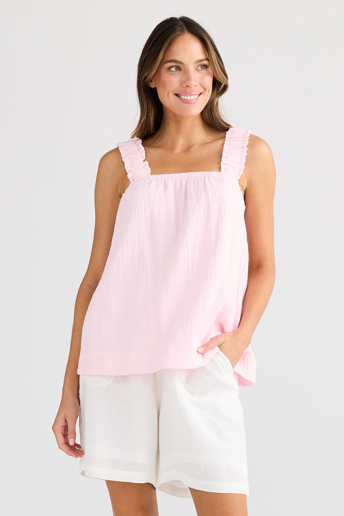Woman wearing a pink sleeveless top and white shorts on a white background