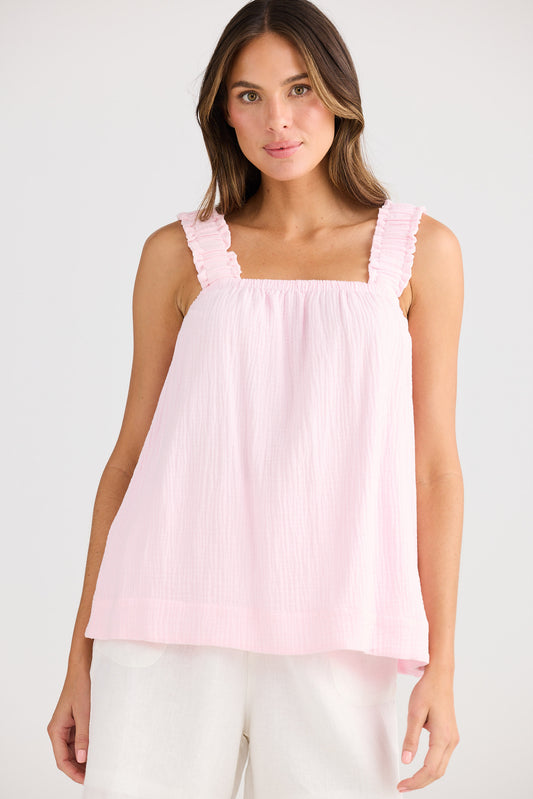 Woman wearing a light pink sleeveless top with ruffled straps on a white background