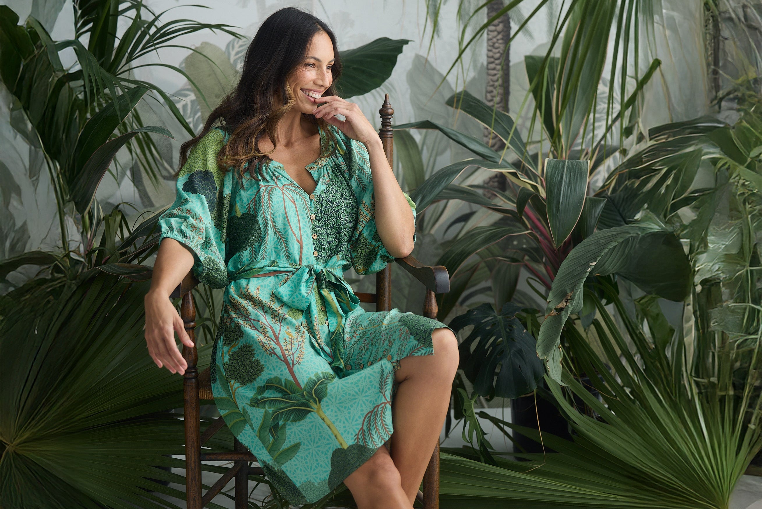 Woman in a green tropical inspired patterned dress sitting among tropical plants