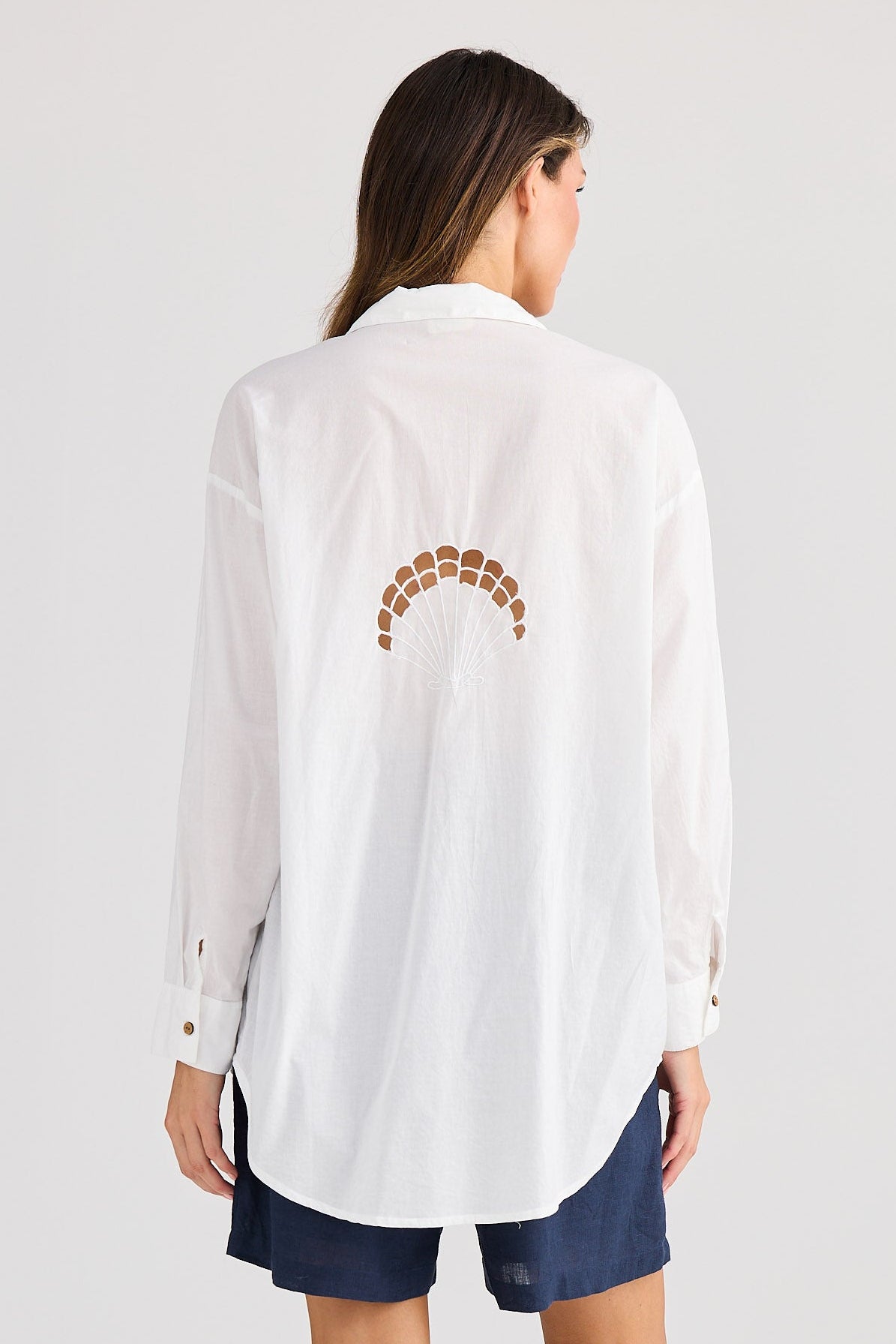 Woman wearing a white shirt with a decorative back design on a plain background