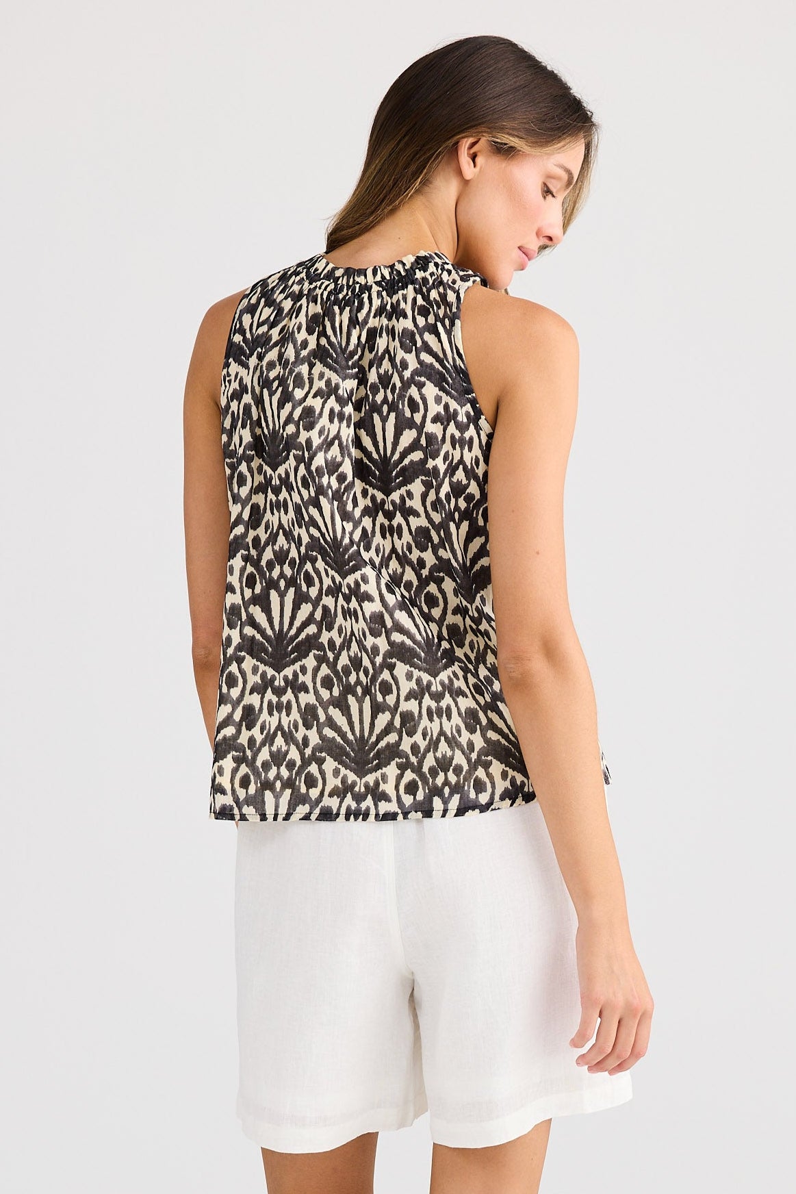 Woman wearing a sleeveless patterned top and white shorts on a plain background