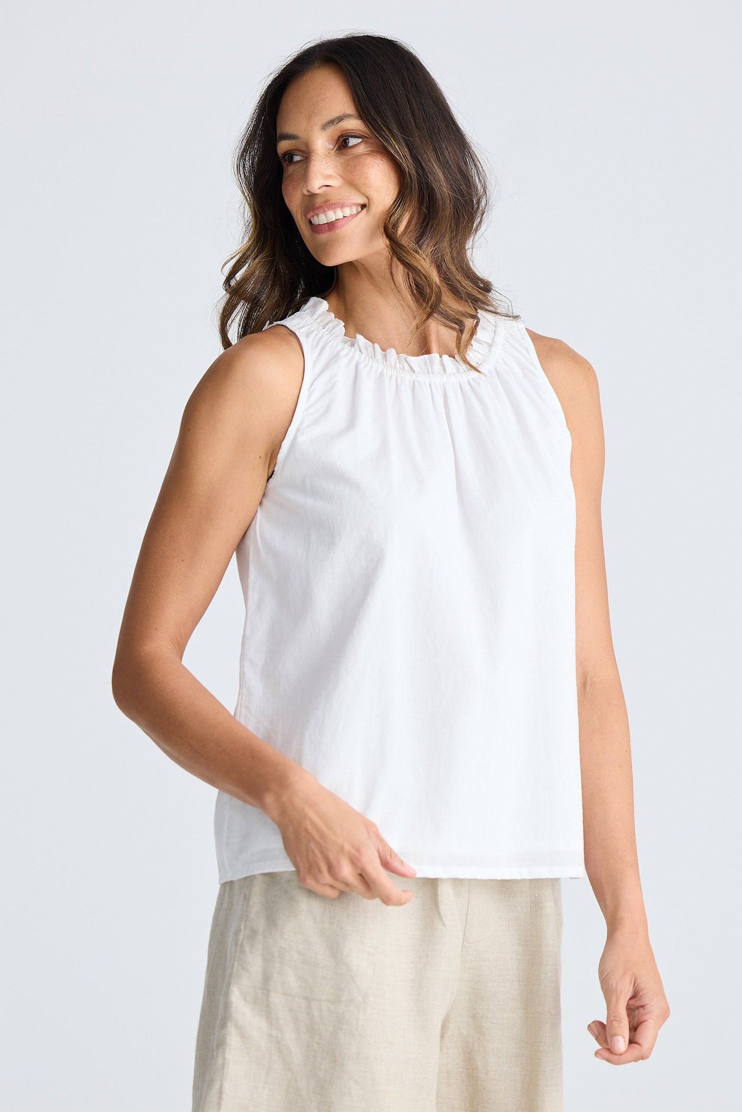 Woman wearing a white sleeveless top and beige skirt on a white background