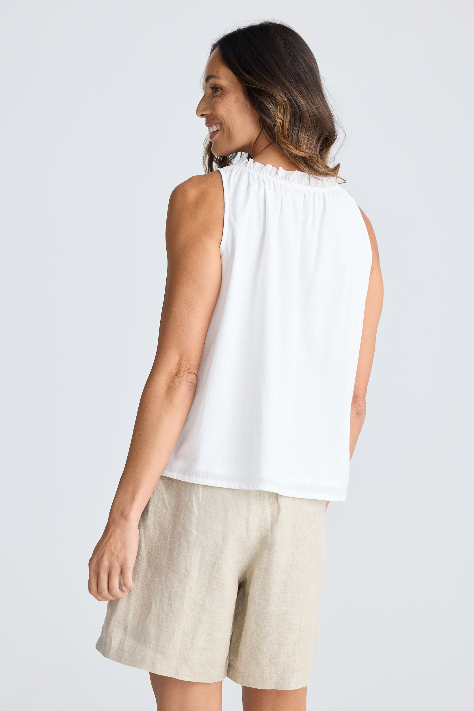 Woman wearing a white sleeveless top and beige shorts on a white background