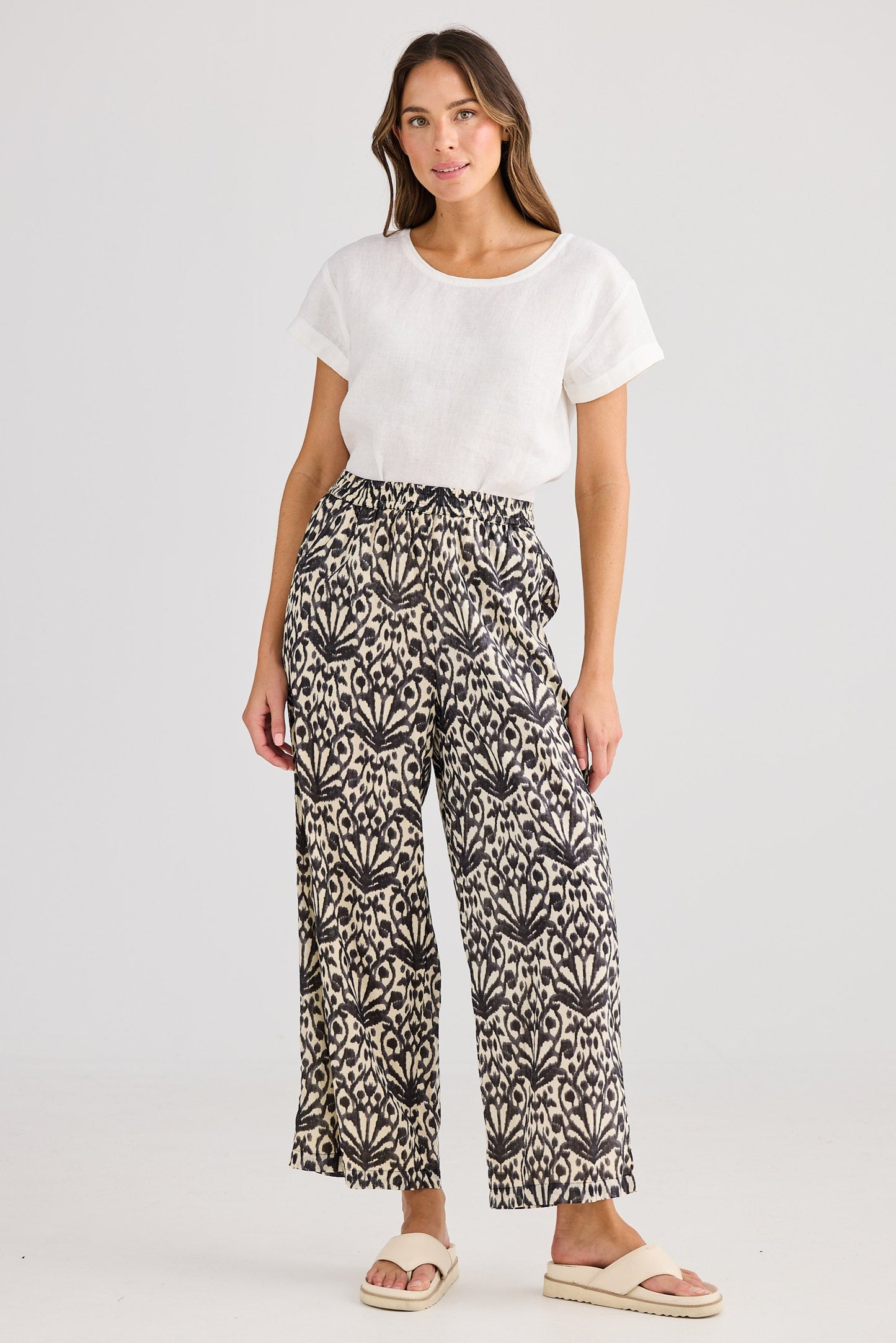 Woman wearing a white top and patterned pants on a plain background