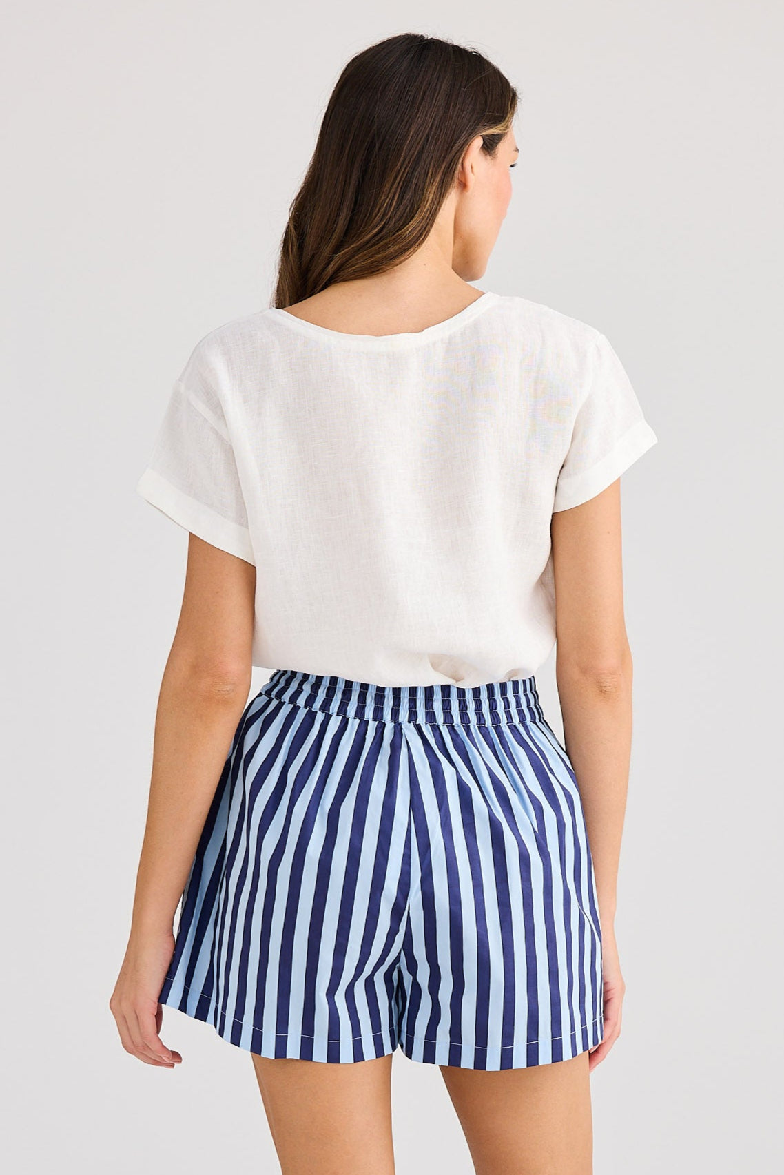Woman wearing a white top and blue striped shorts on a light gray background