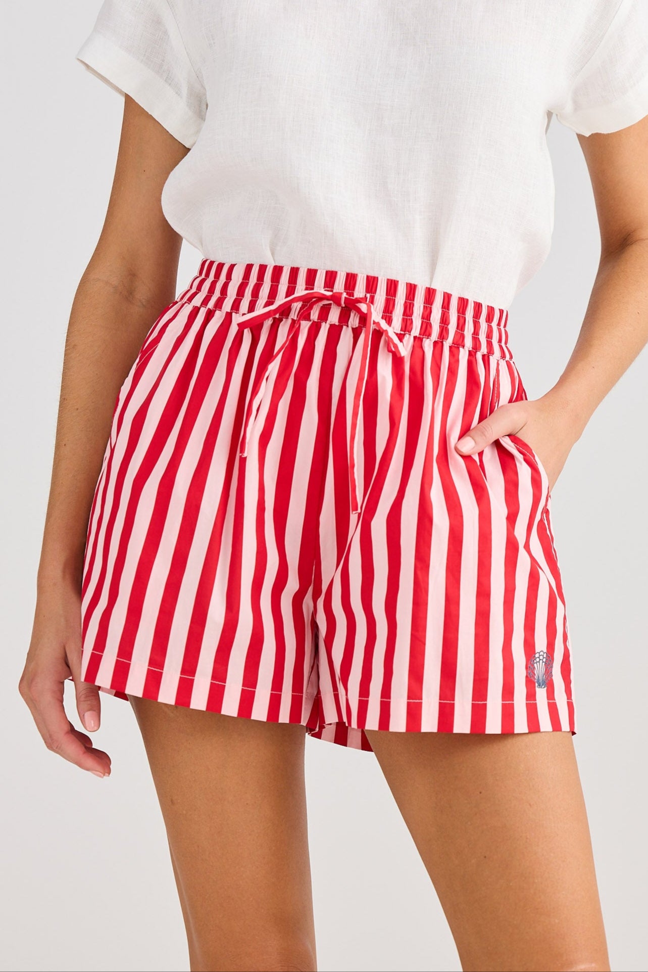 Woman wearing a white top and red striped shorts on a plain background