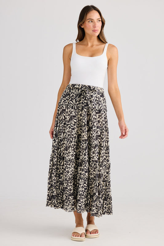 Woman wearing a white tank top and patterned skirt on a plain background