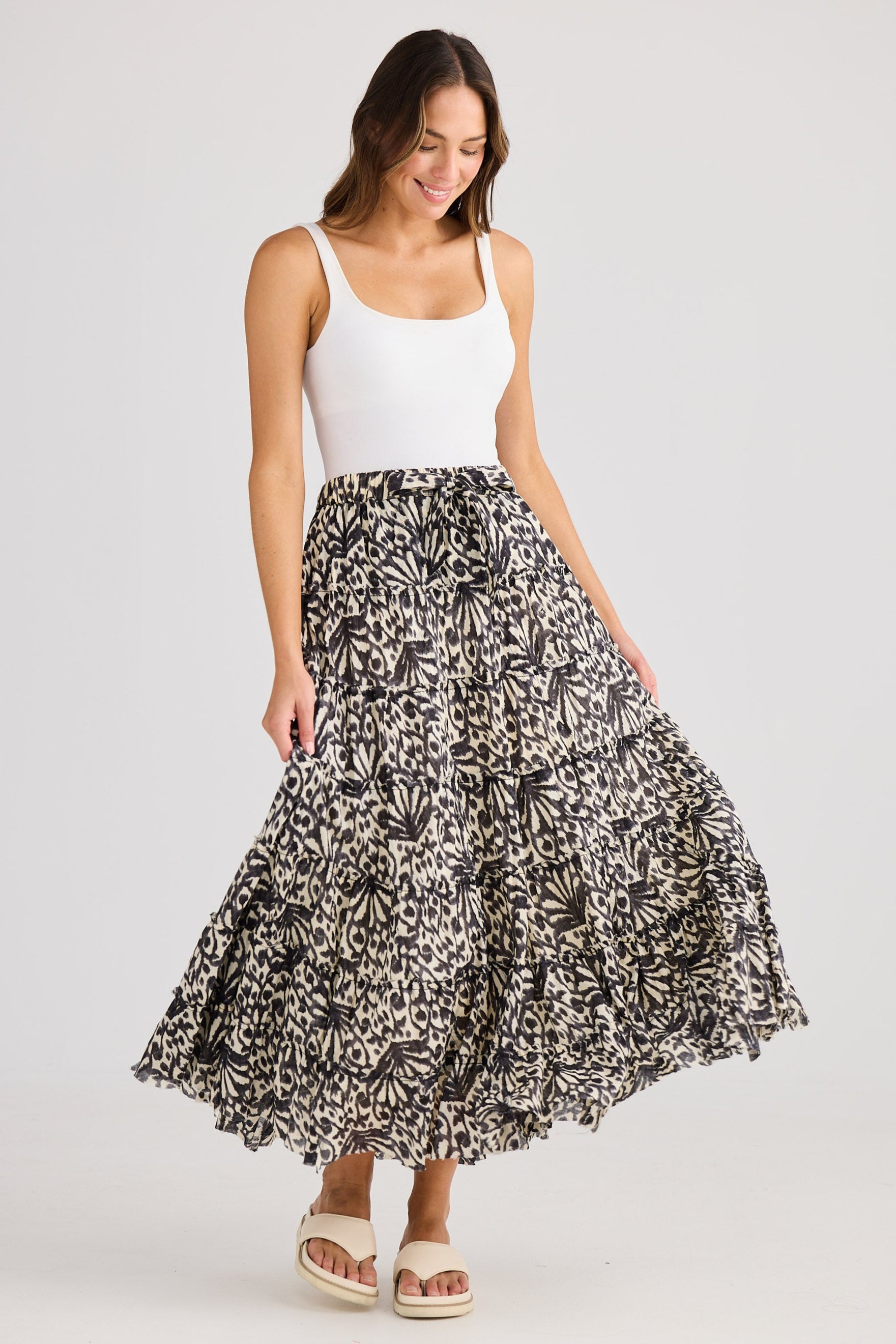 Woman wearing a white top and black and white patterned skirt on a plain background