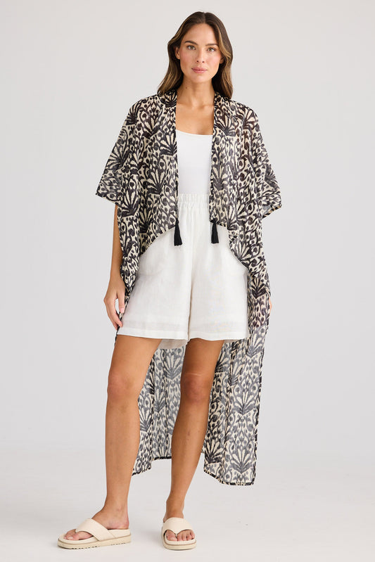Woman wearing a patterned kimono over a white outfit on a plain background