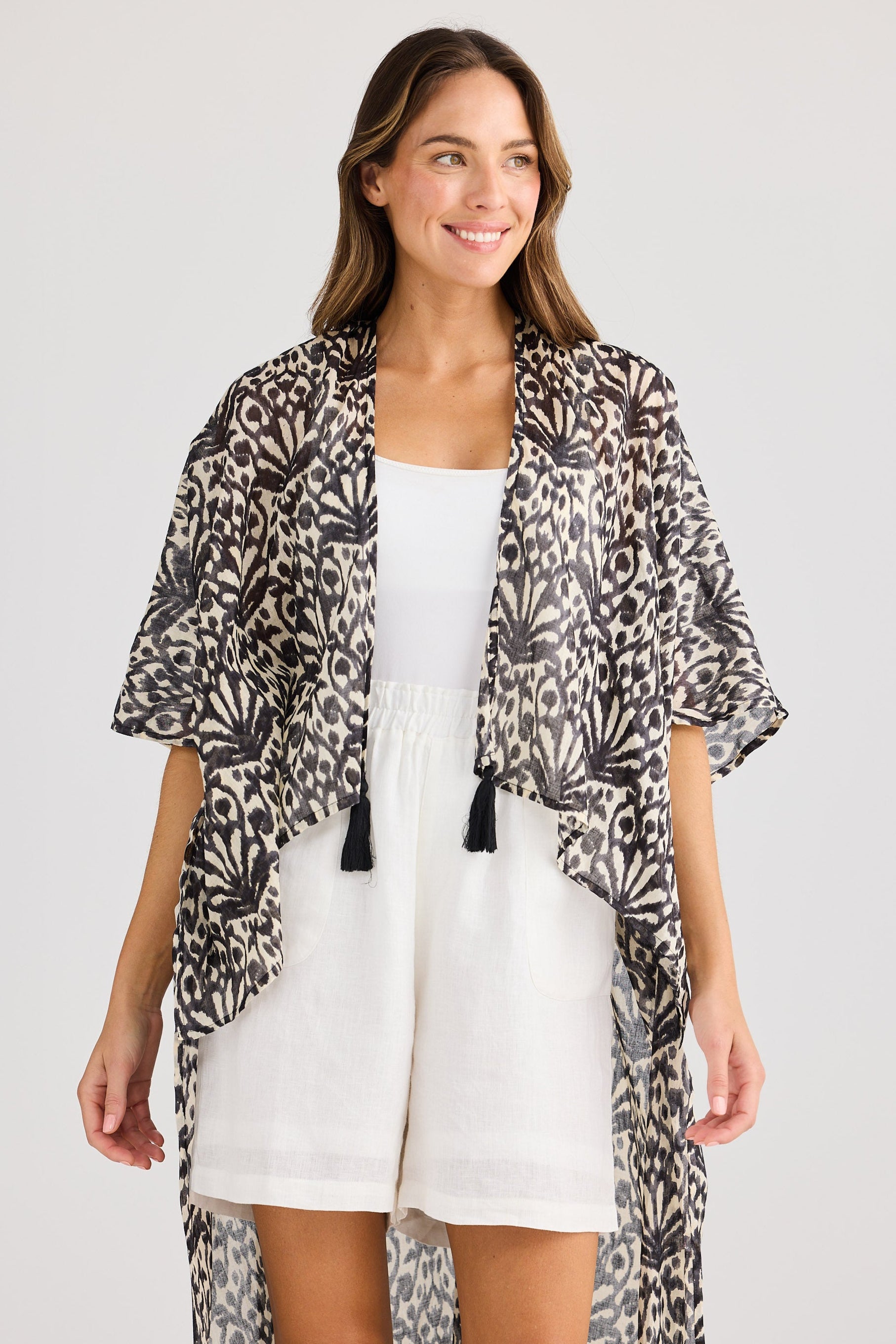 Woman wearing a leopard print kimono over a white dress on a plain background