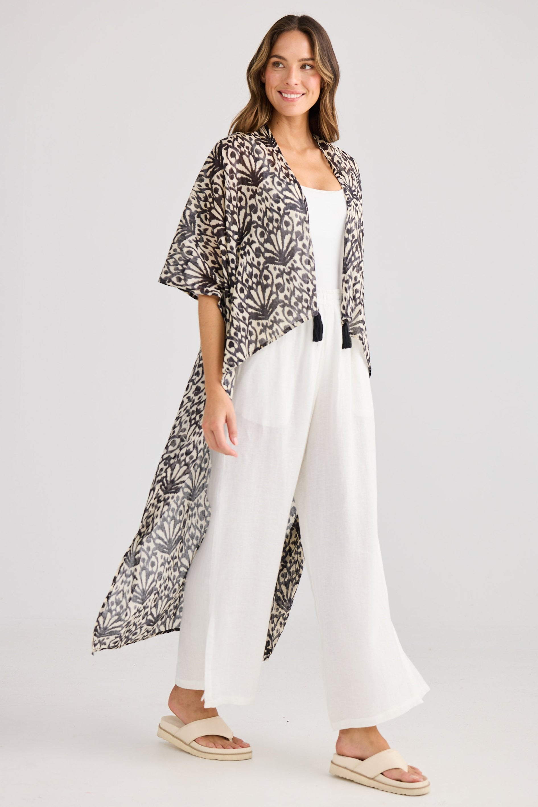 Woman wearing a patterned kimono-style jacket over a white outfit on a plain background