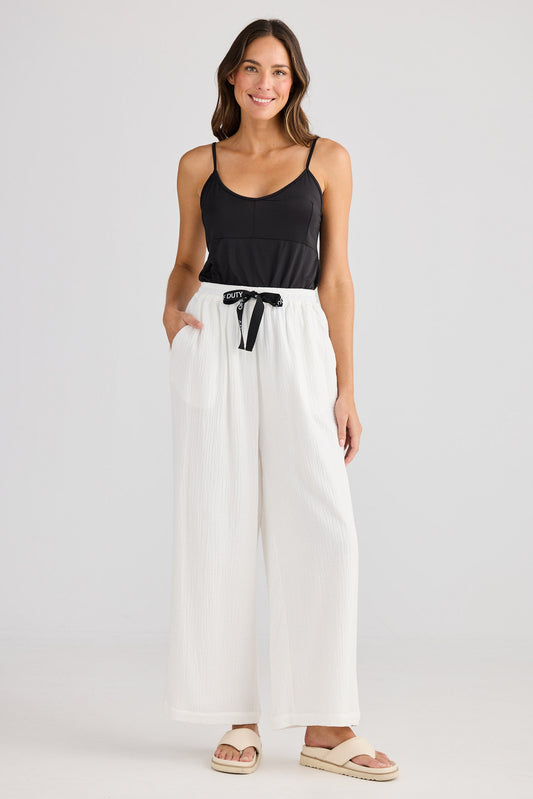 Woman wearing a black tank top and white wide-leg pants on a plain background