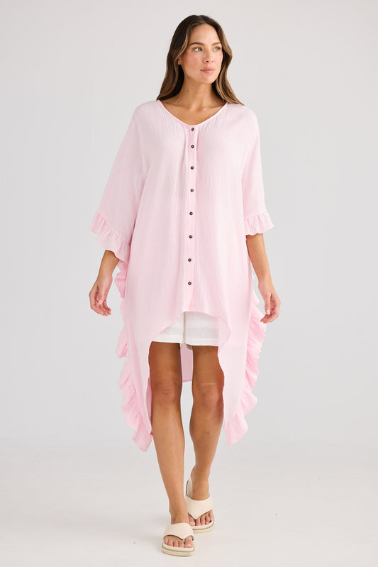 Woman wearing a light pink beach cover-up over a white dress on a plain background
