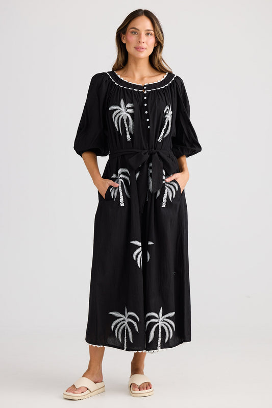 Woman wearing a black dress with white palm tree patterns on a white background