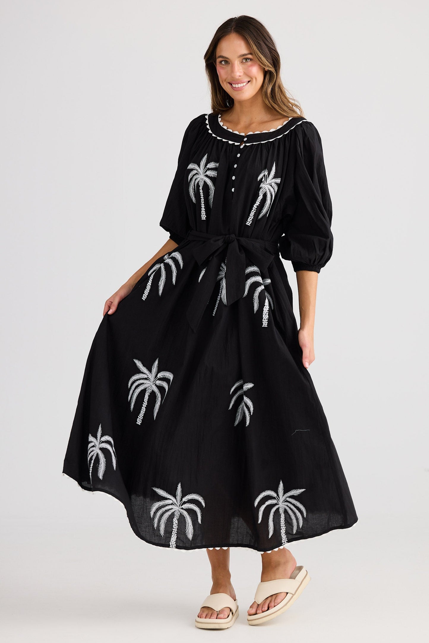 Woman wearing a black dress with white palm tree patterns on a plain background