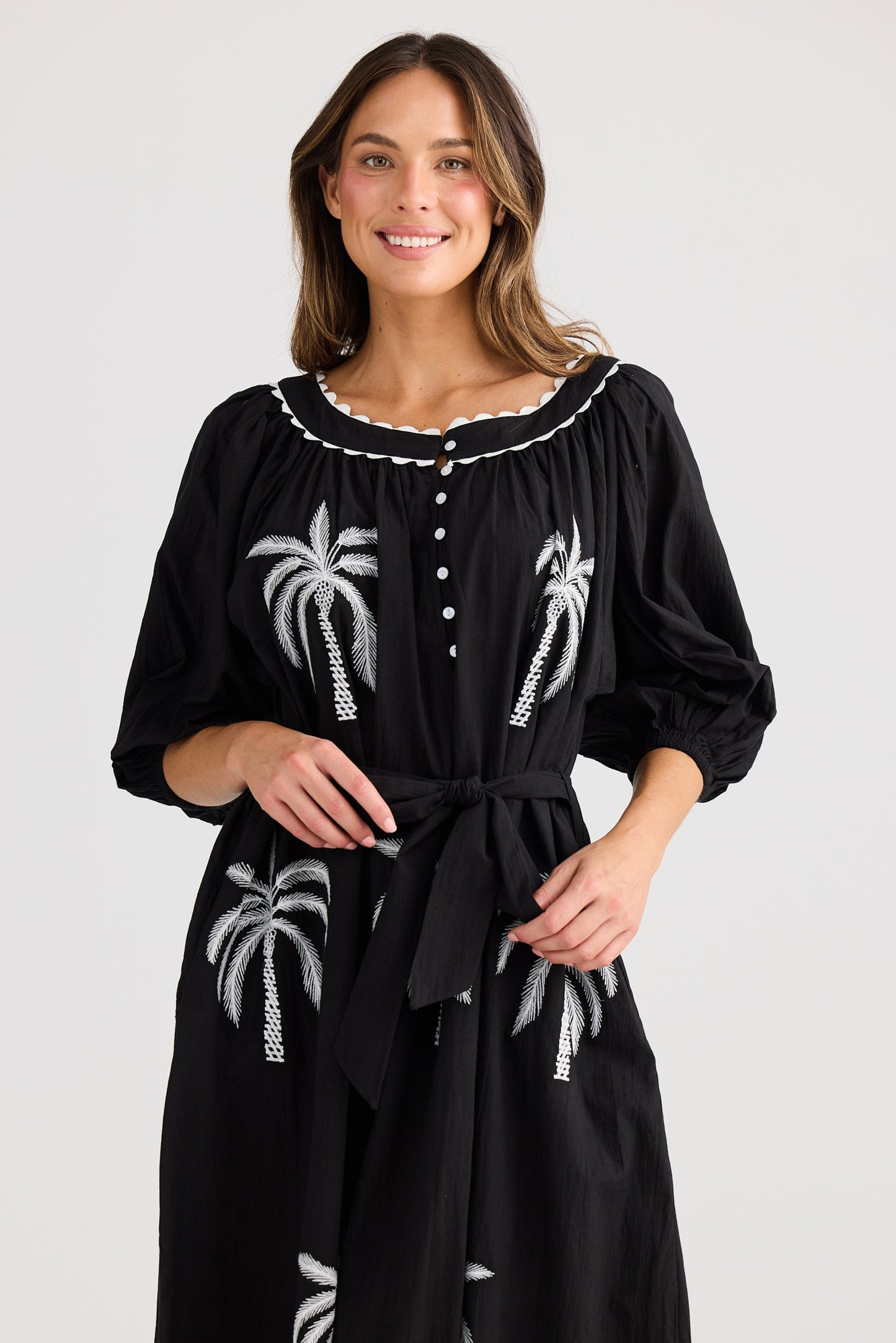 Woman wearing a black dress with white palm tree patterns on a plain background