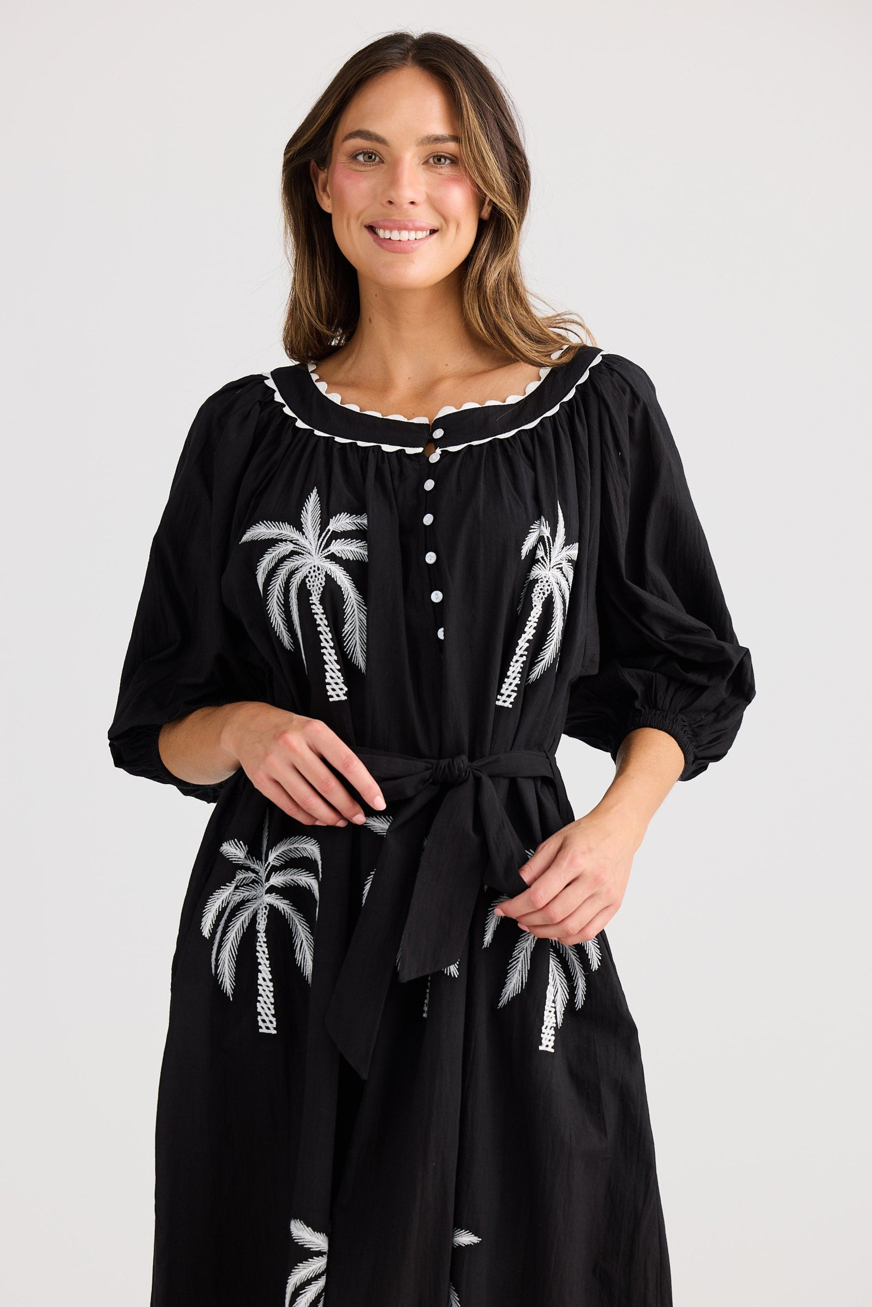 Woman wearing a black dress with white palm tree patterns on a plain background