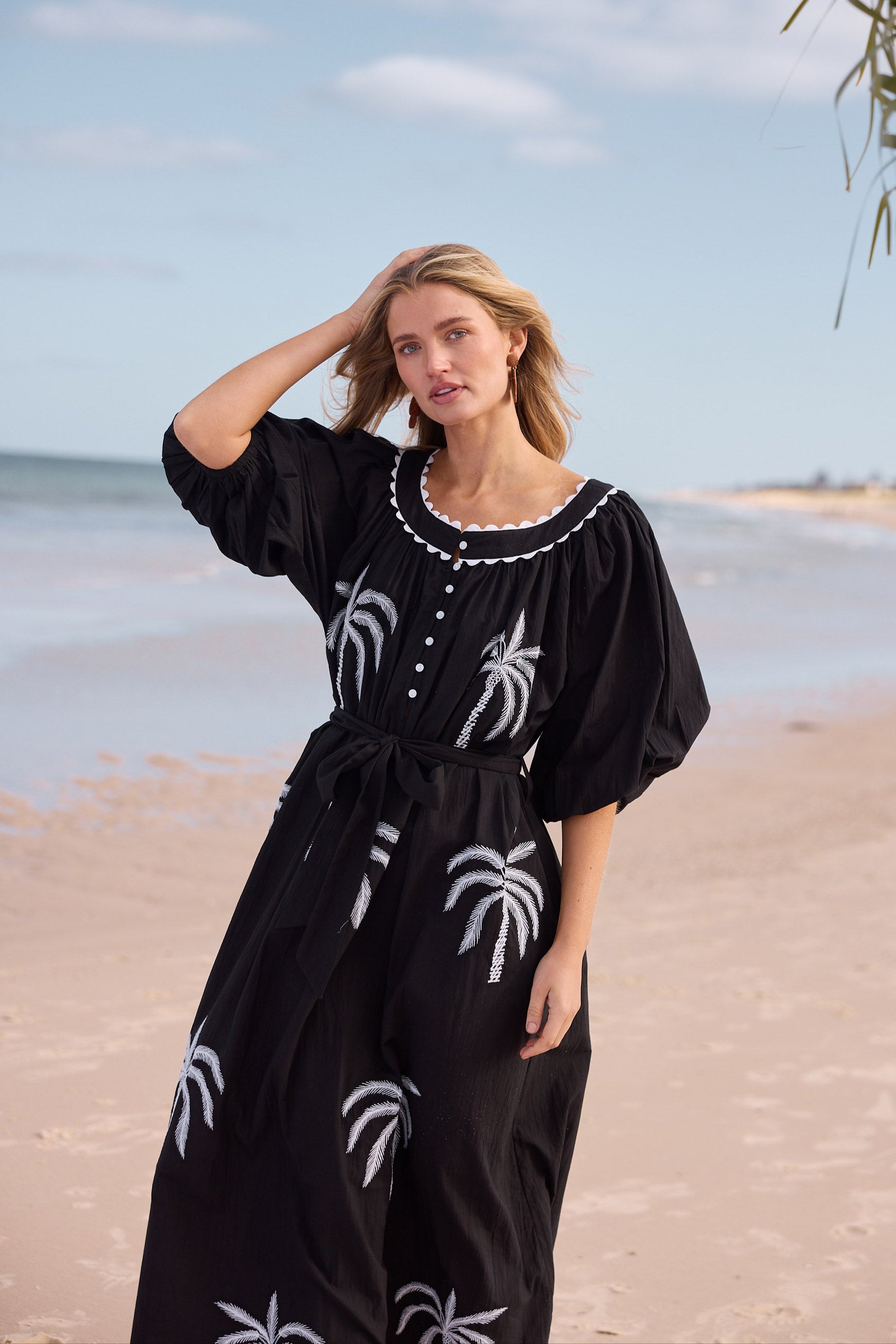 Woman in a black dress with palm tree patterns on a beach