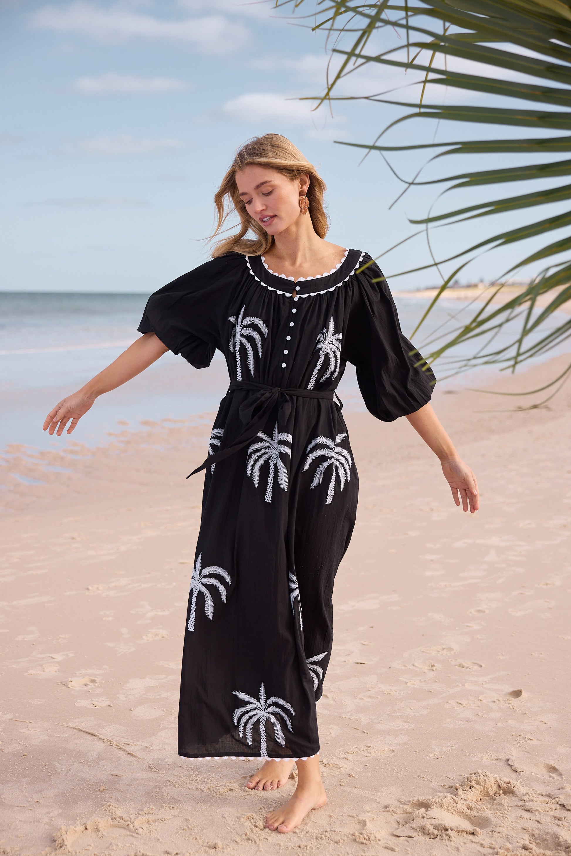 Woman in a black dress with palm tree patterns on a beach