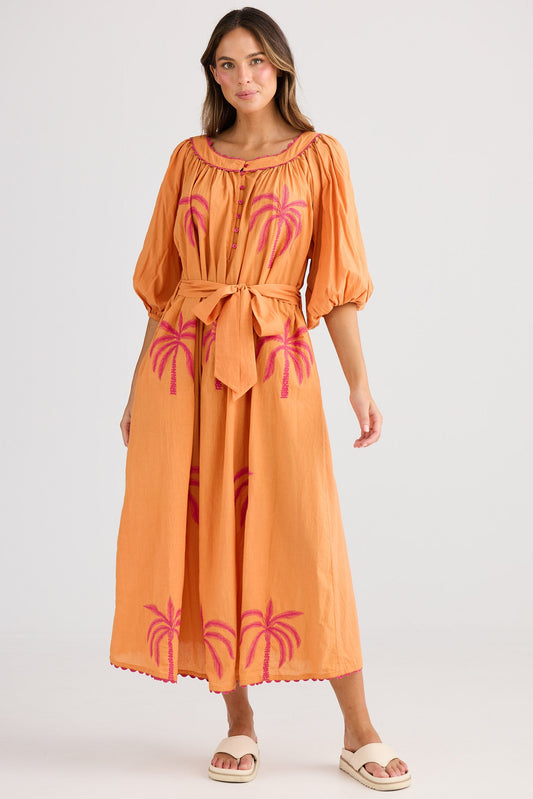 Woman wearing an orange dress with pink palm tree designs on a white background