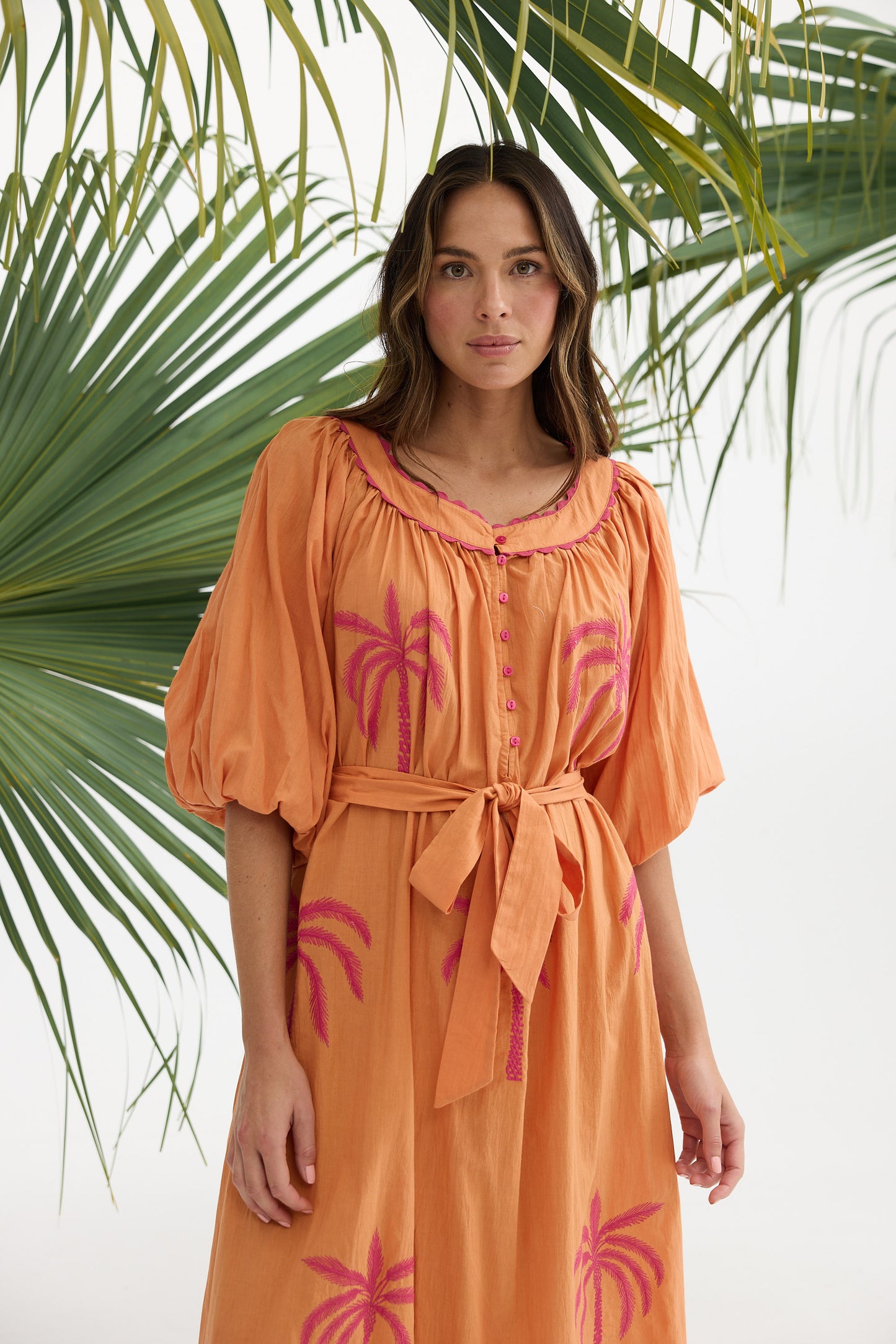 Woman wearing an orange dress with pink palm tree designs against a white background