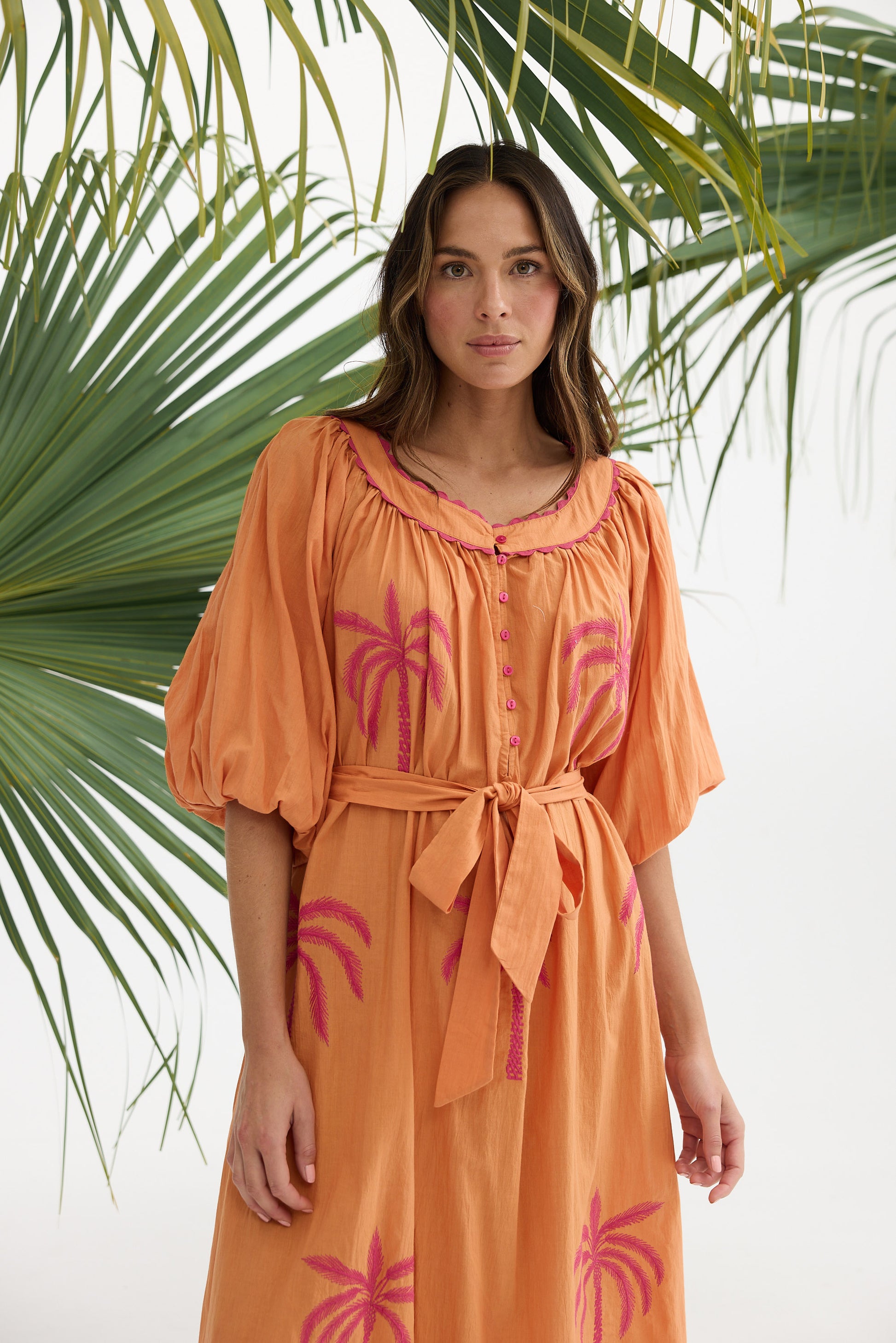 Woman wearing an orange dress with pink palm tree designs against a white background