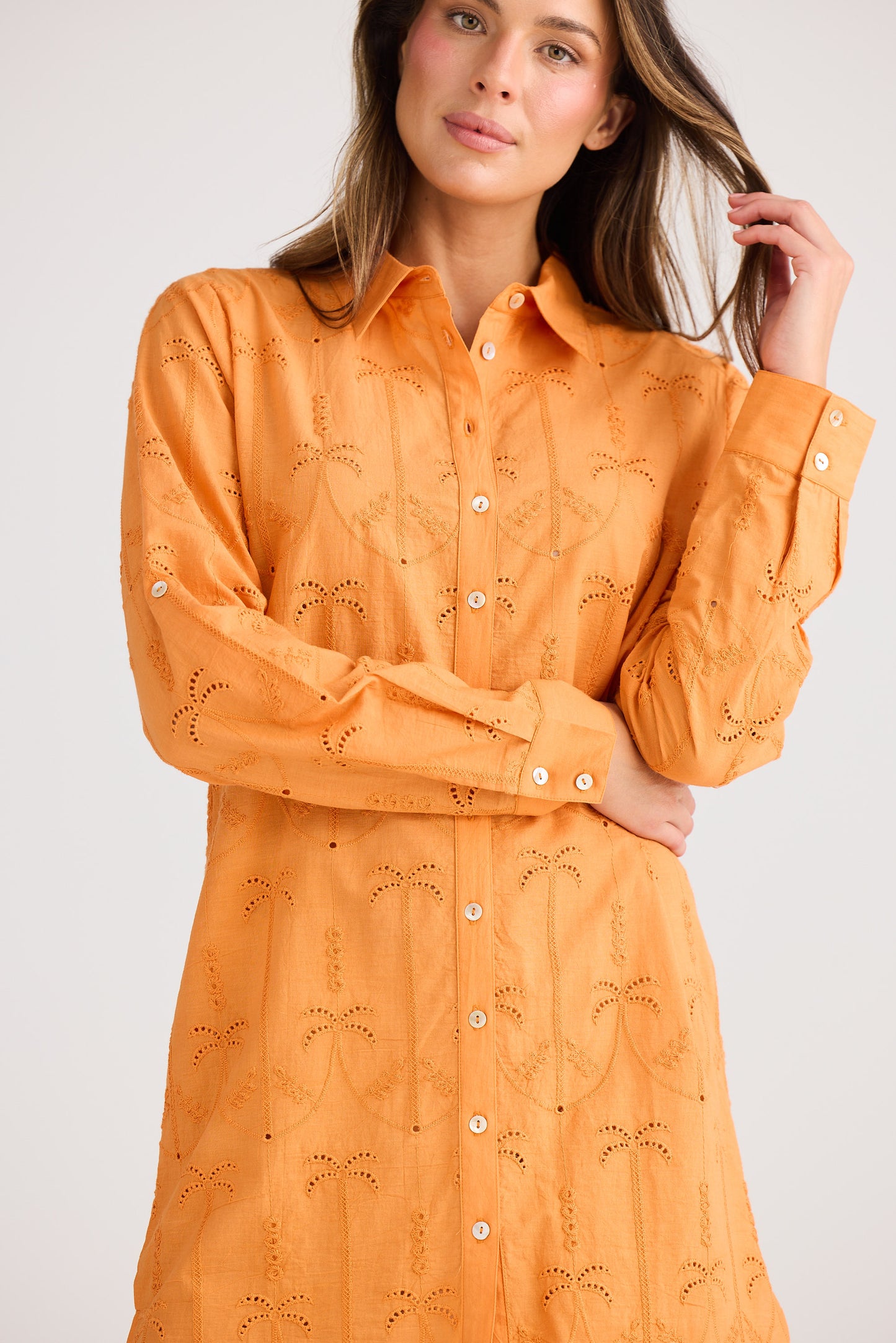 Woman wearing an orange embroidered shirt against a white background