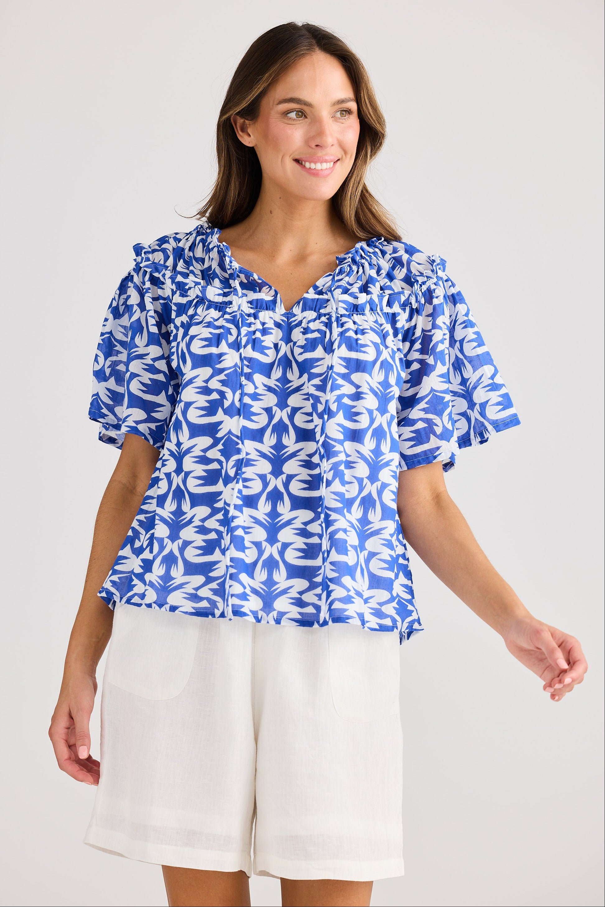 Woman wearing a blue floral blouse and white shorts on a light gray background