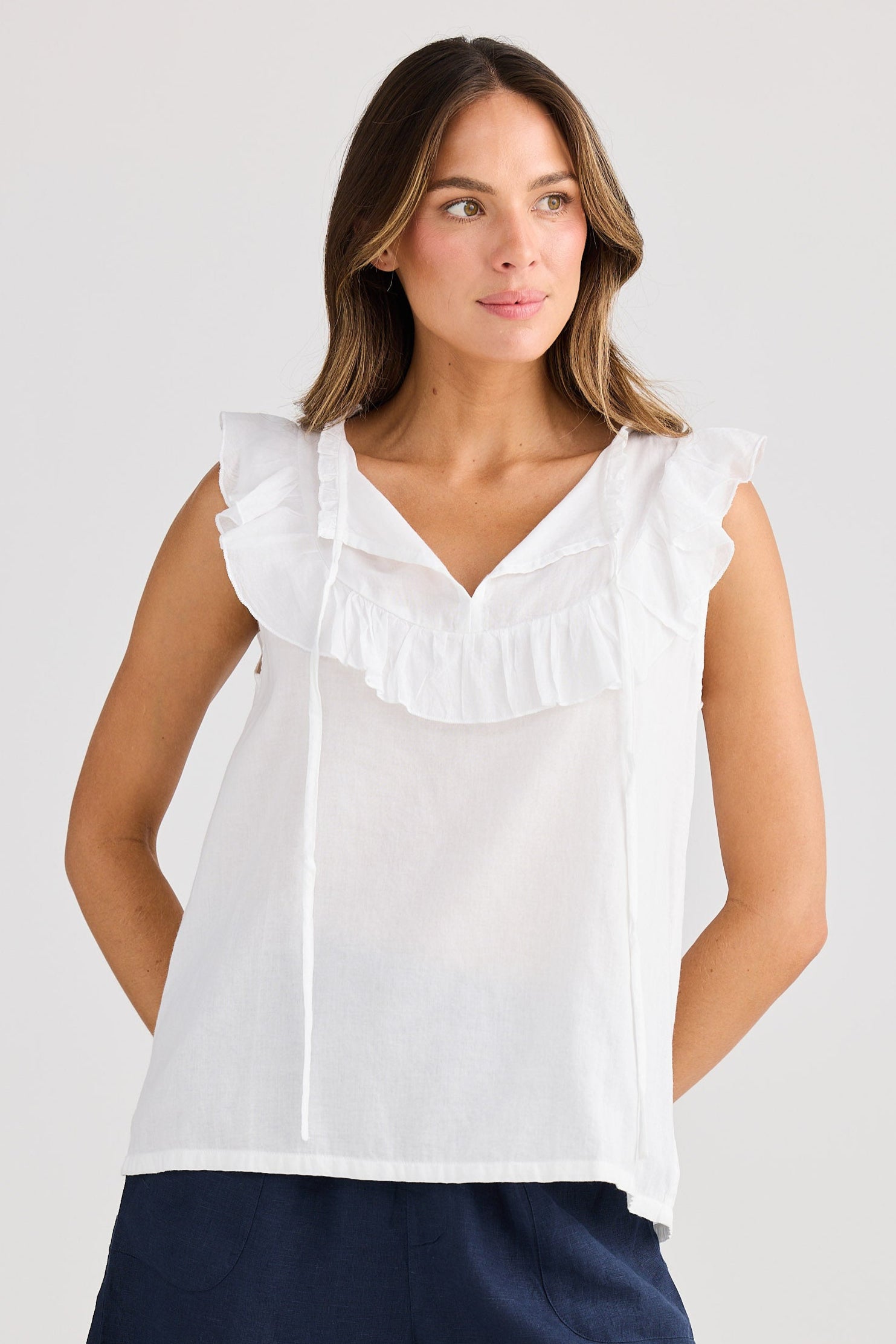 Woman wearing a white blouse with ruffled details and navy shorts on a plain background
