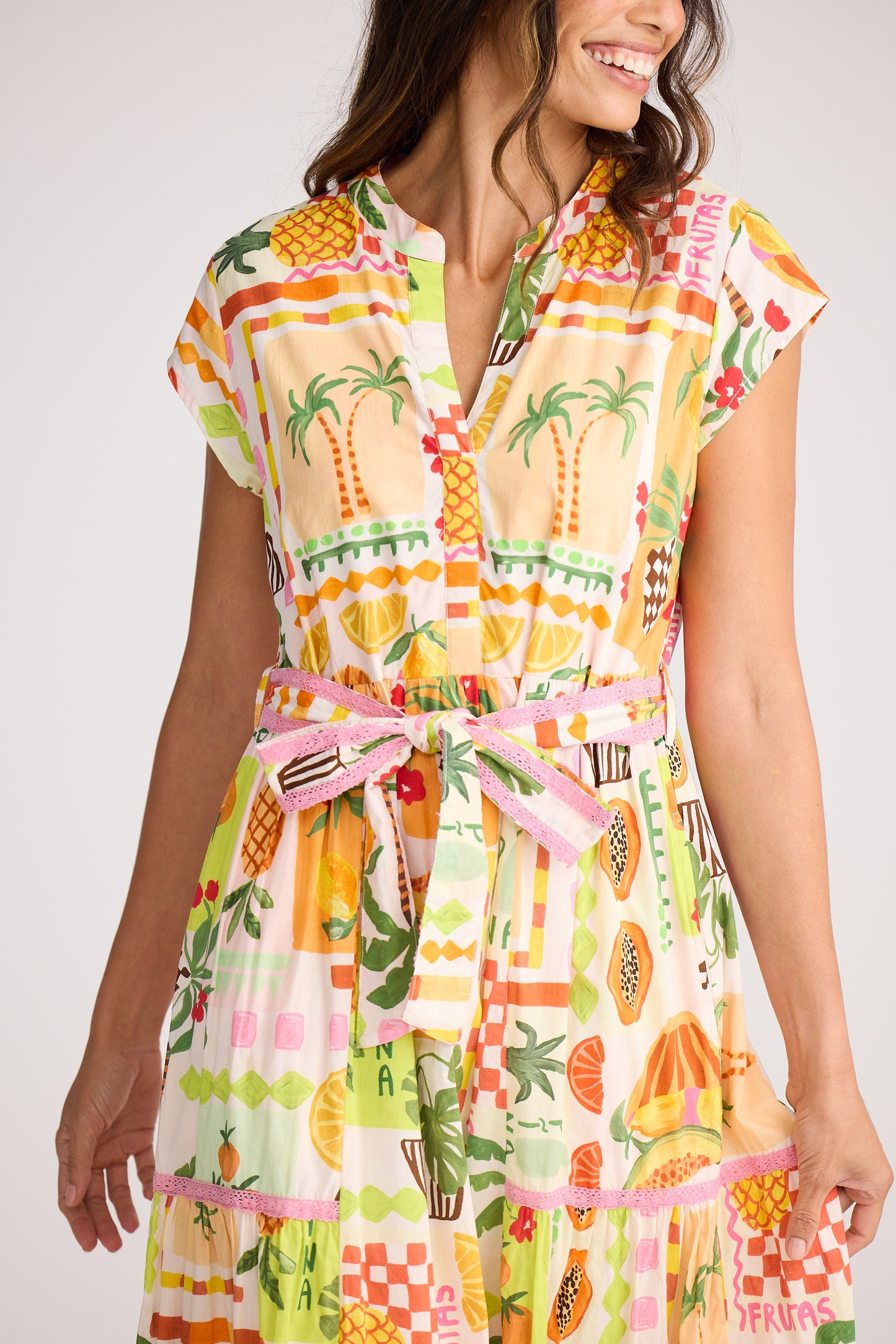 Woman wearing a colorful dress with fruit and palm tree pattern on a white background