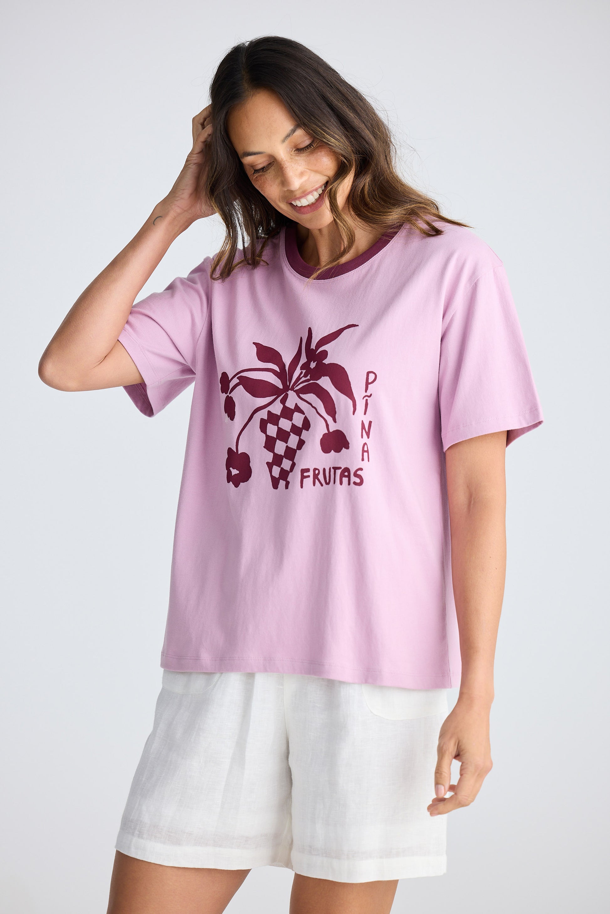 Woman wearing a pink t-shirt with a graphic design and text, standing against a plain background