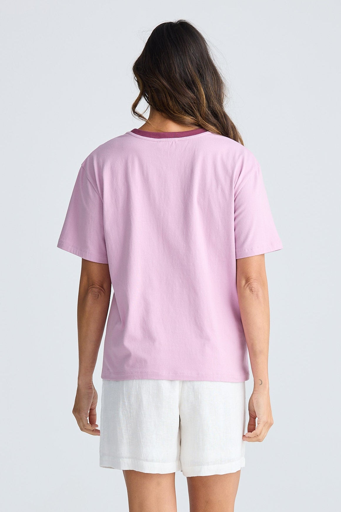 Person wearing a pink t-shirt and white shorts on a light gray background